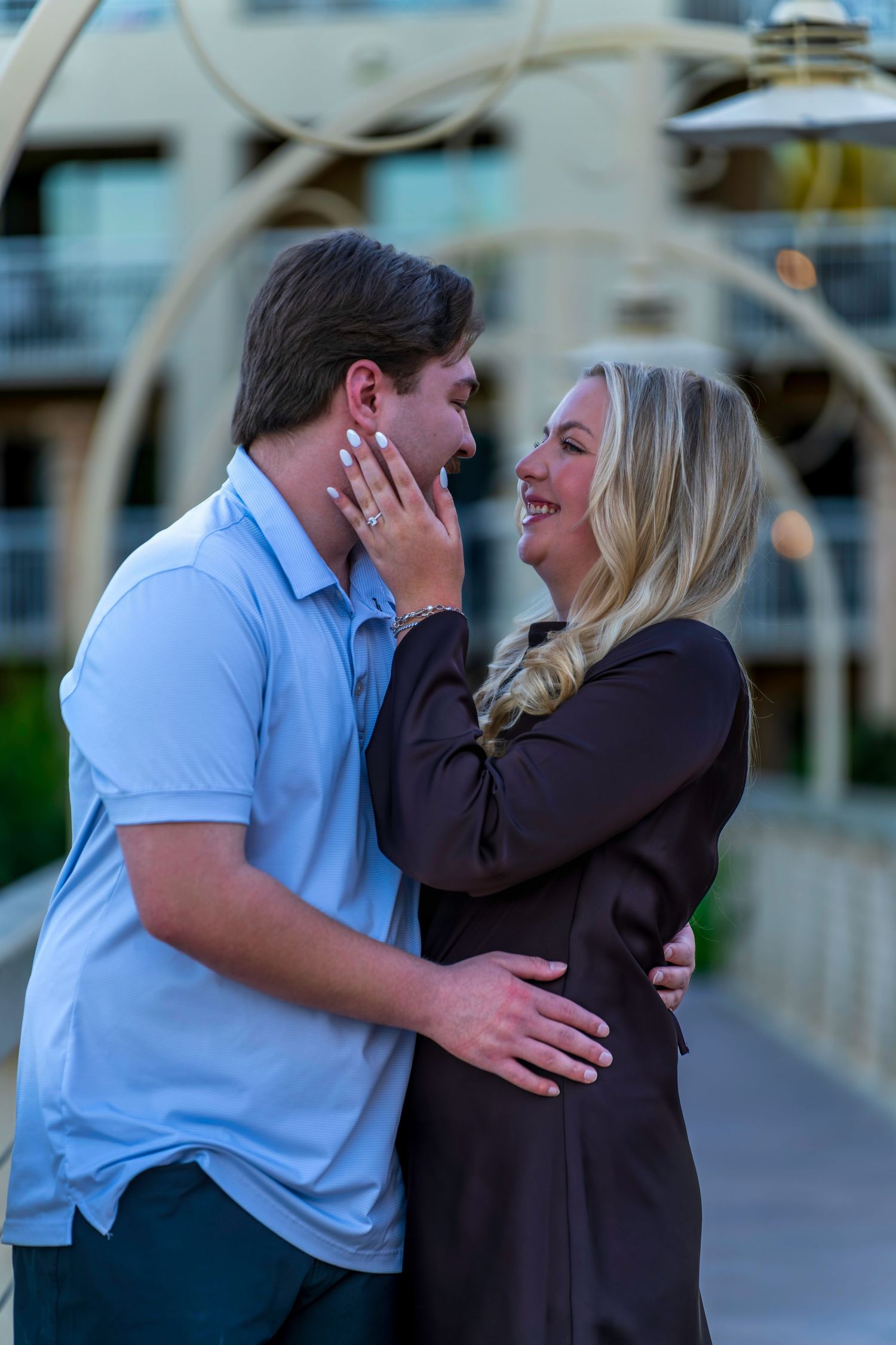 Joyful couple embracing and smiling during an outdoor engagement moment, woman showing off her new ring.