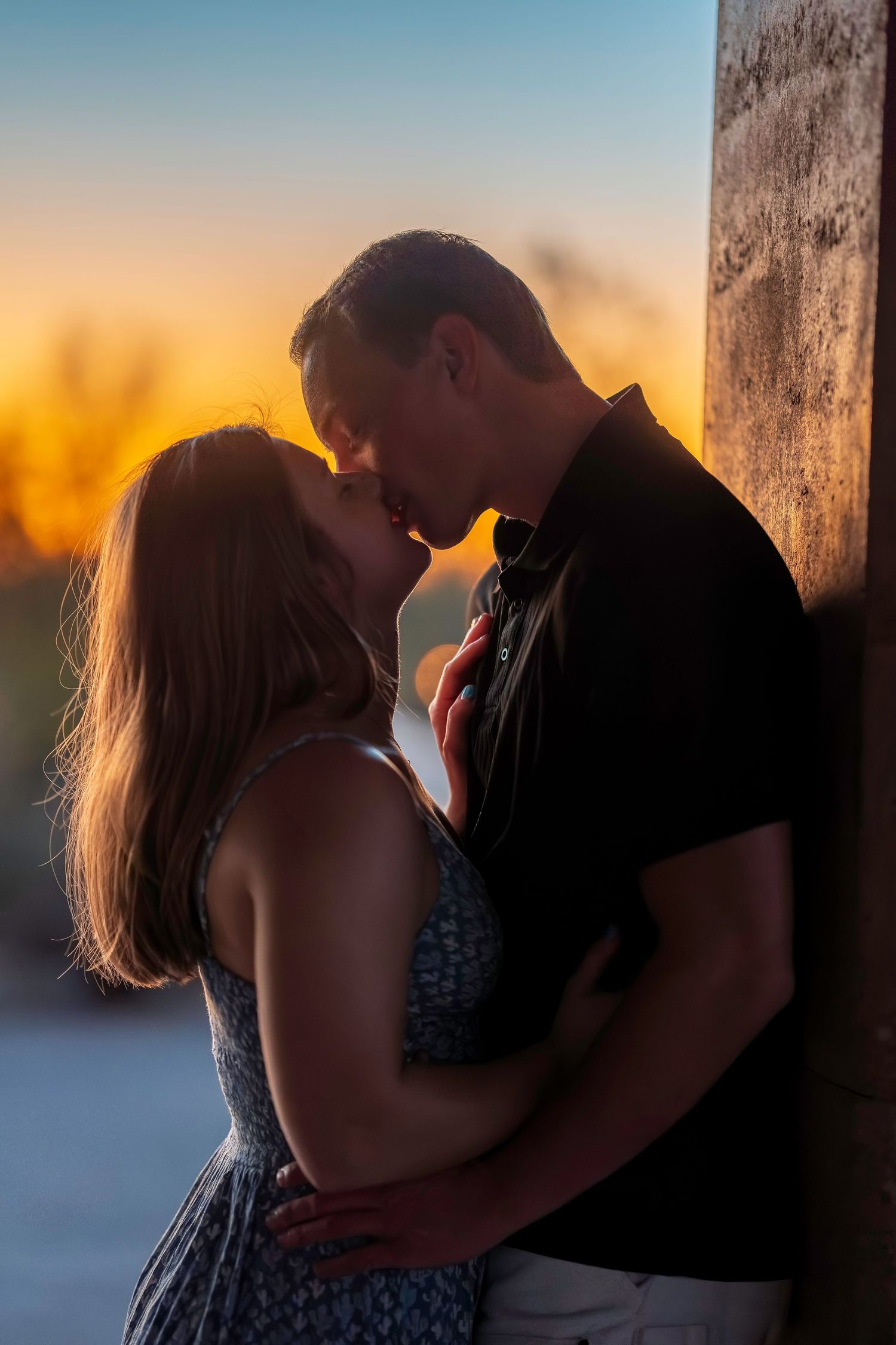 Romantic couple kissing at golden sunset leaning against stone wall.