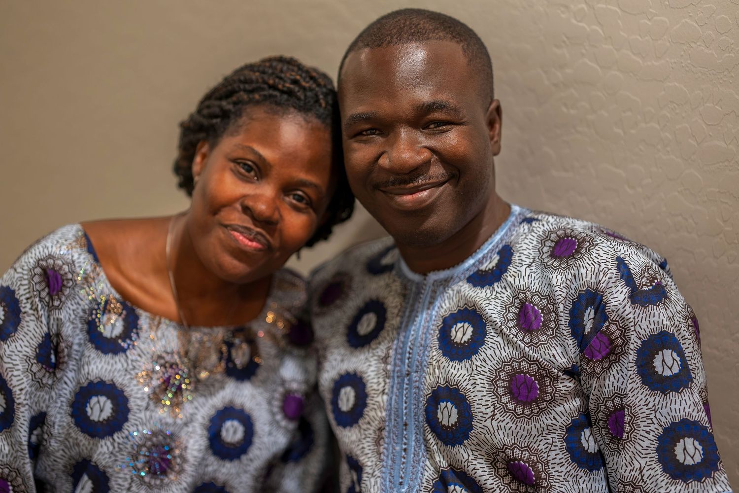 A smiling couple wearing matching African print attire poses together for a portrait photo.