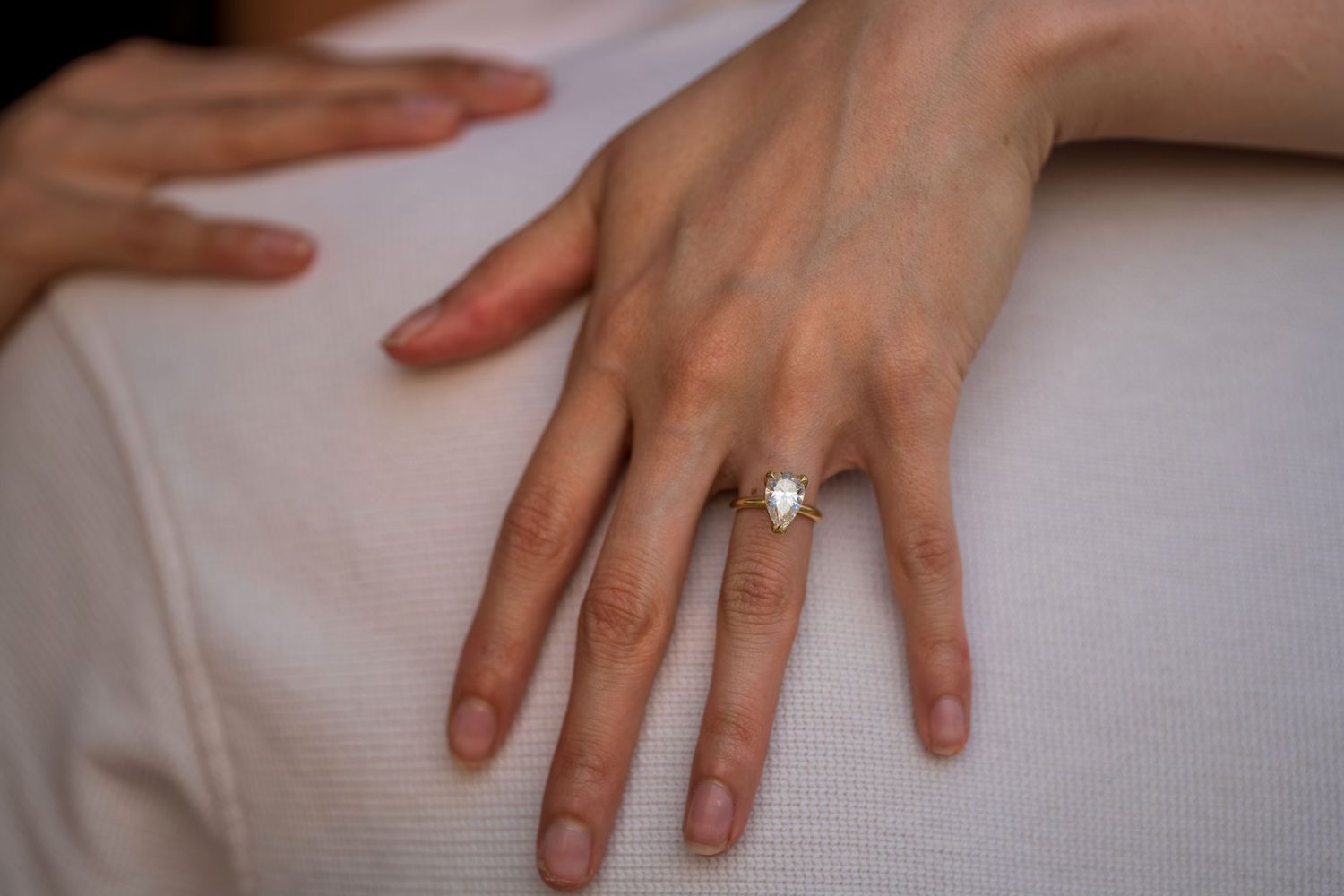 Close-up of elegant diamond engagement ring on womans hand resting on white fabric.