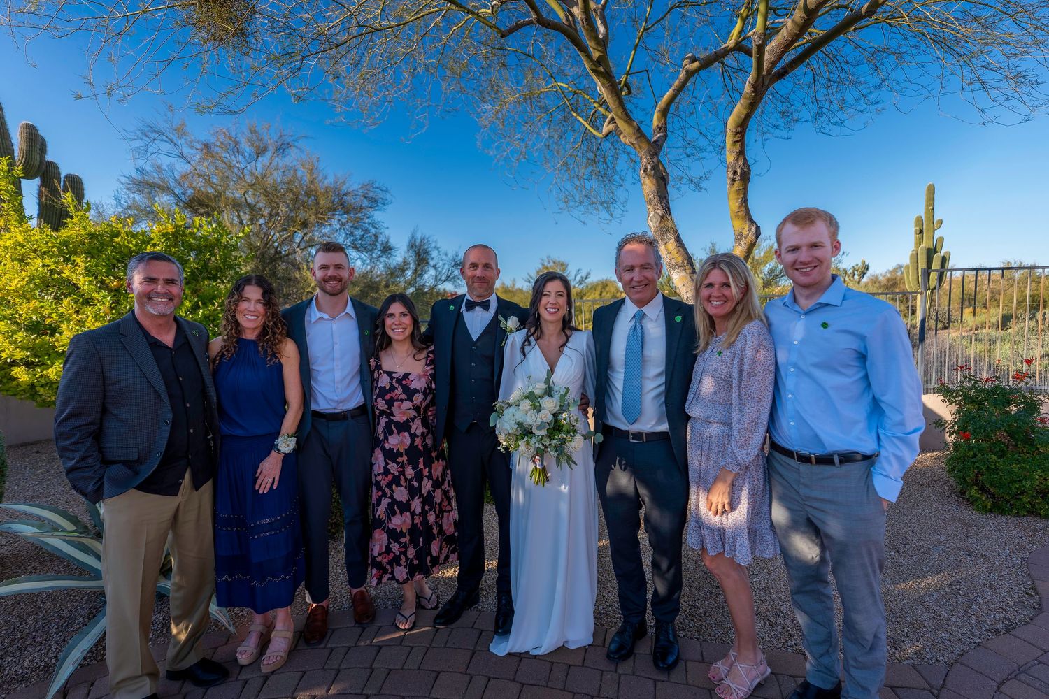 Wedding party group portrait with bride and groom surrounded by guests in desert landscape setting.