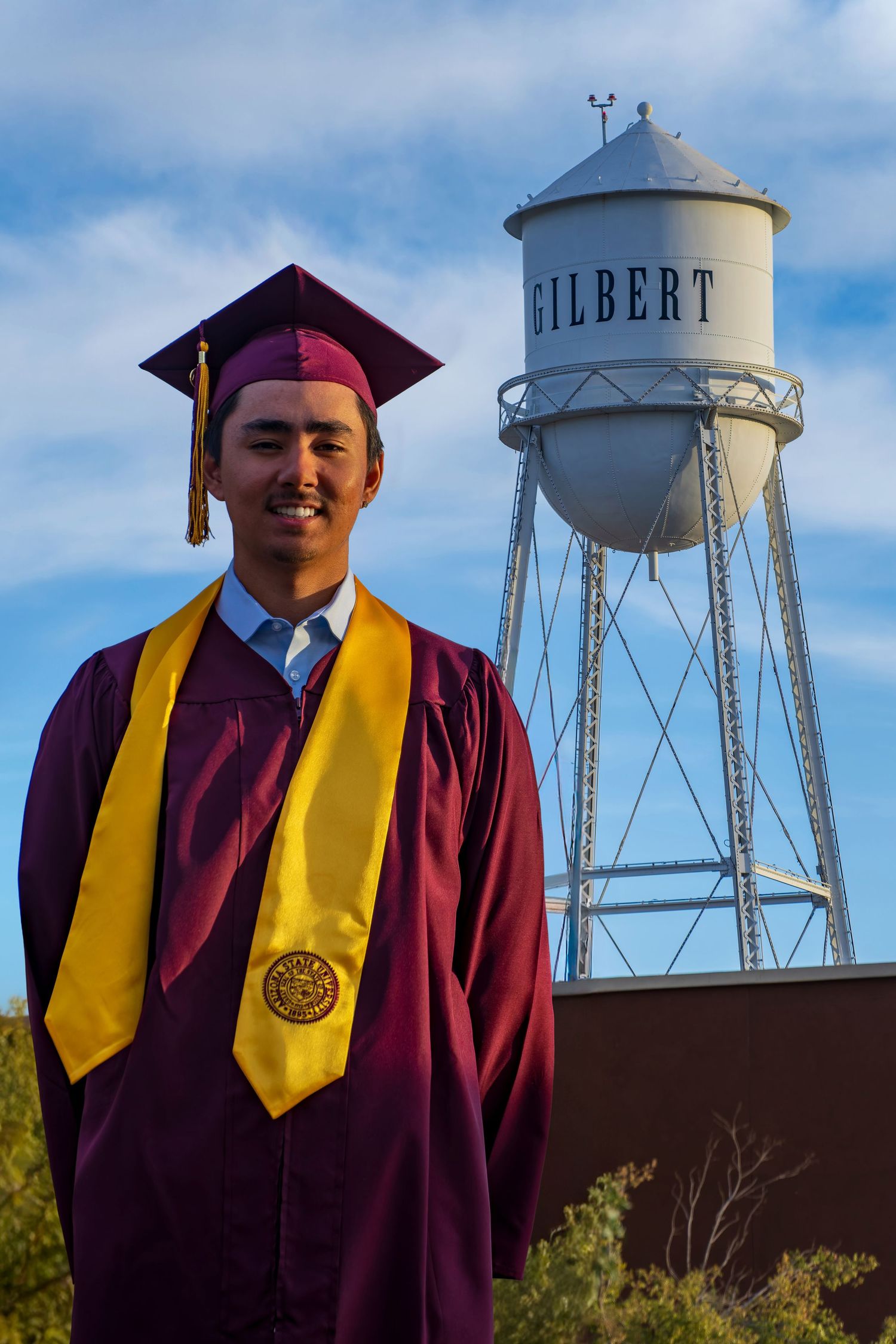 Graduate in academic regalia poses in front of Gilbert water tower.
