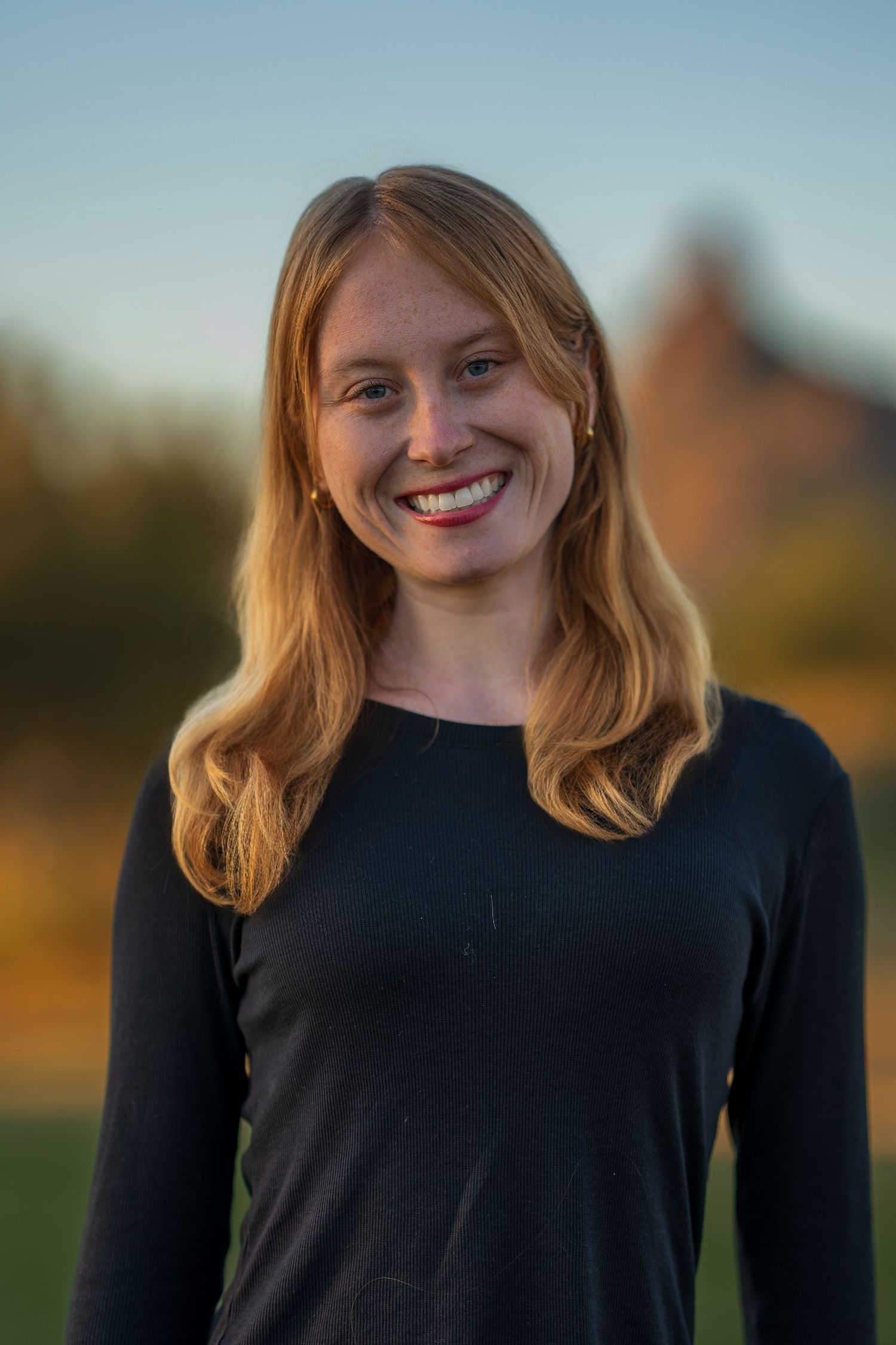 Portrait of person in black long sleeve top with blonde hair against natural background.