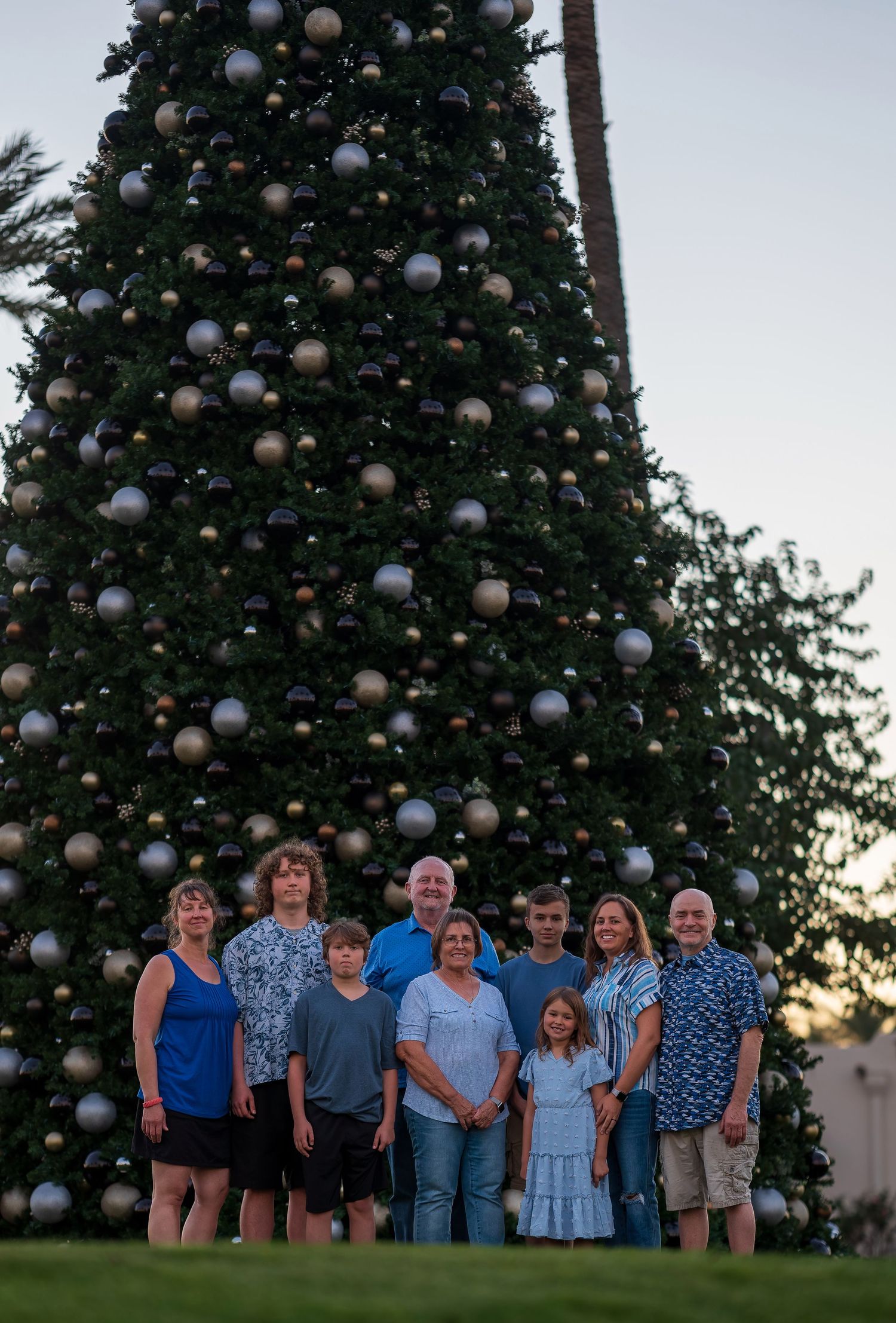 Family holiday photo in front of large decorated Christmas tree at sunset.