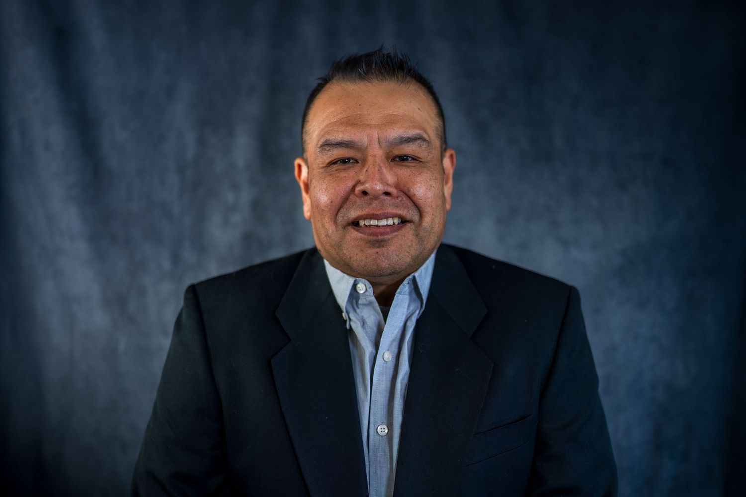 Professional studio portrait against dark textured background with dramatic lighting.