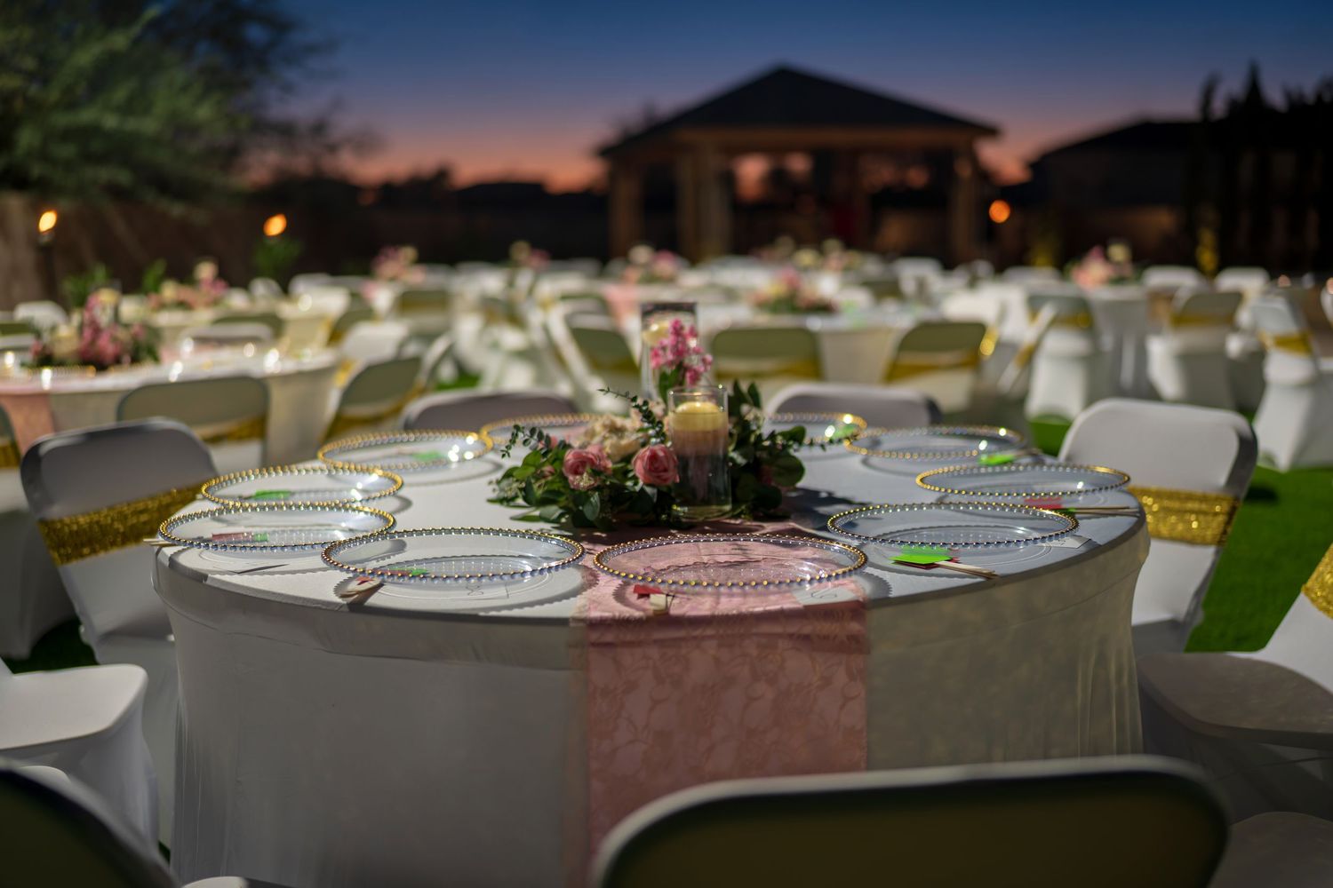 Elegant outdoor dining setup with formal place settings and floral centerpieces at sunset.