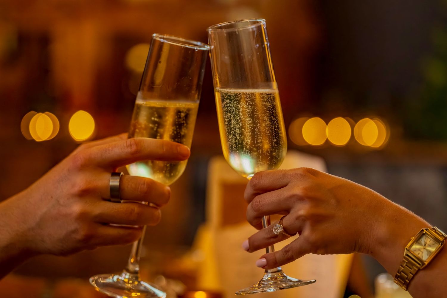 Hands toasting with champagne flutes in a romantic restaurant setting.