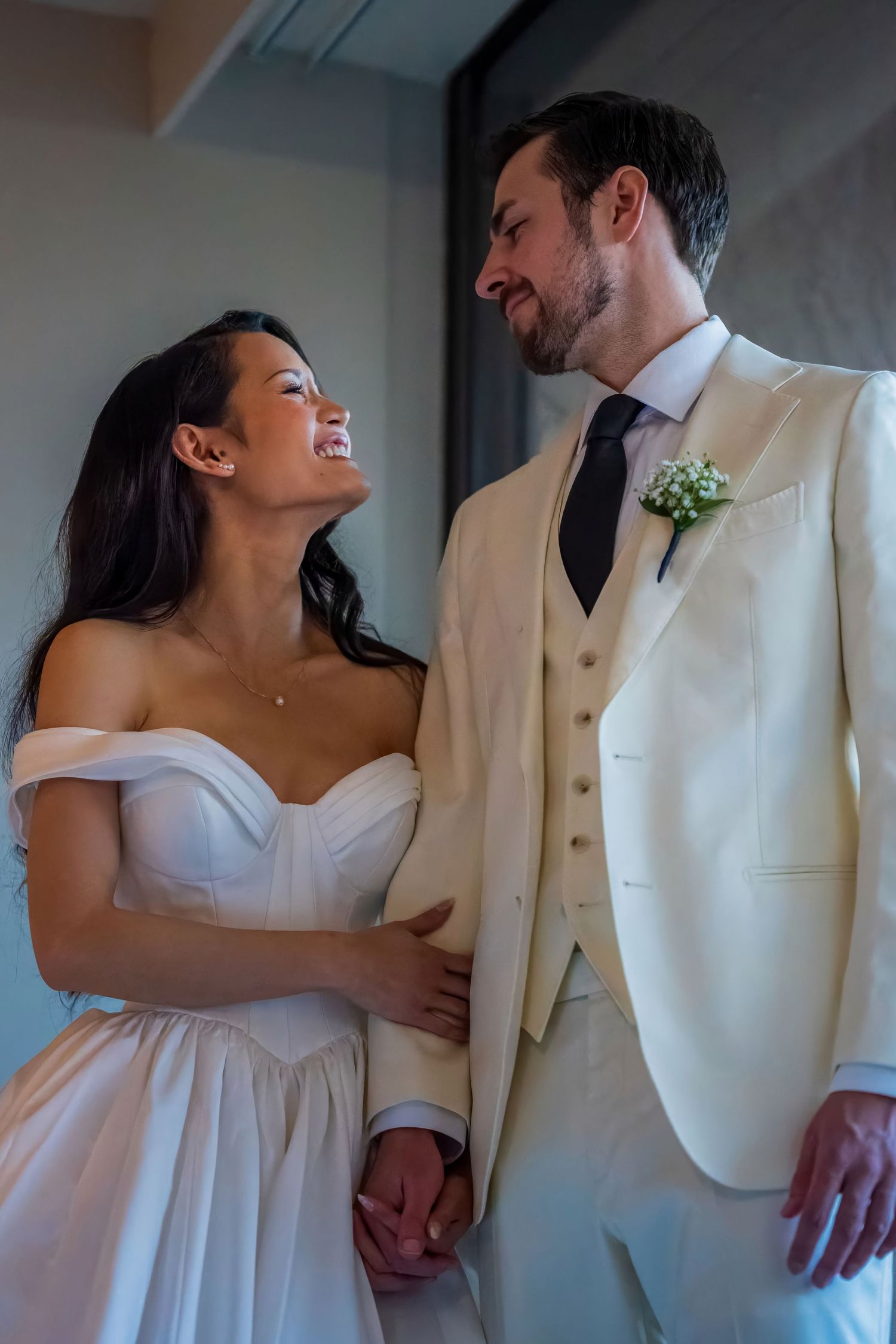 A joyful wedding couple shares a candid moment in cream and white formal attire.