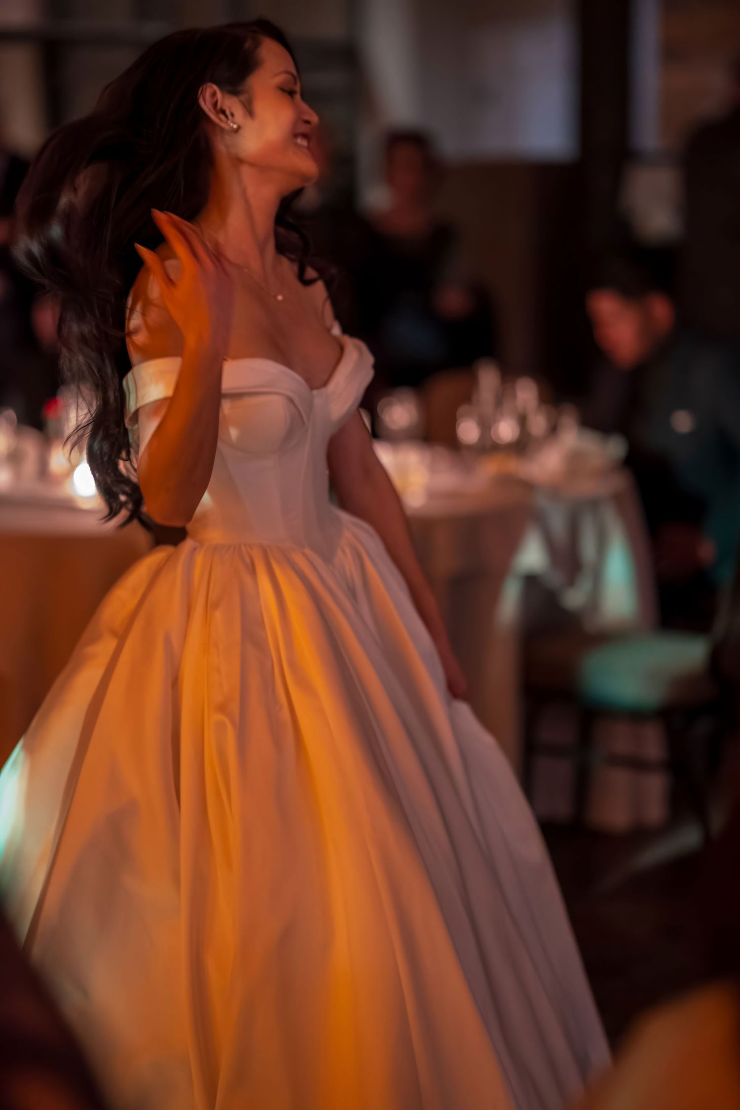 Elegant white wedding dress swirls during dance movement in warm lighting.