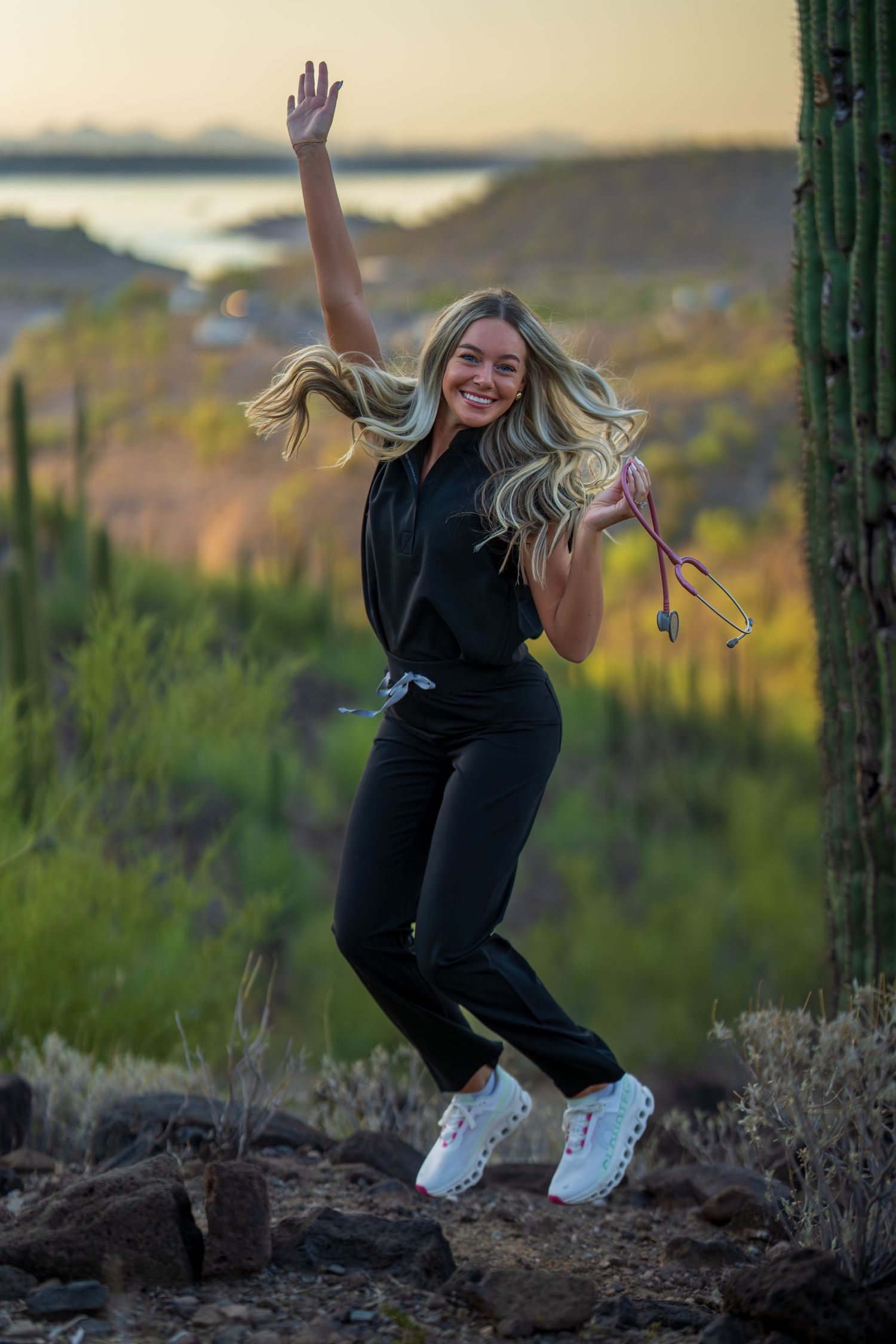 A joyful figure jumps in the desert landscape with saguaro cacti and mountains at sunset.