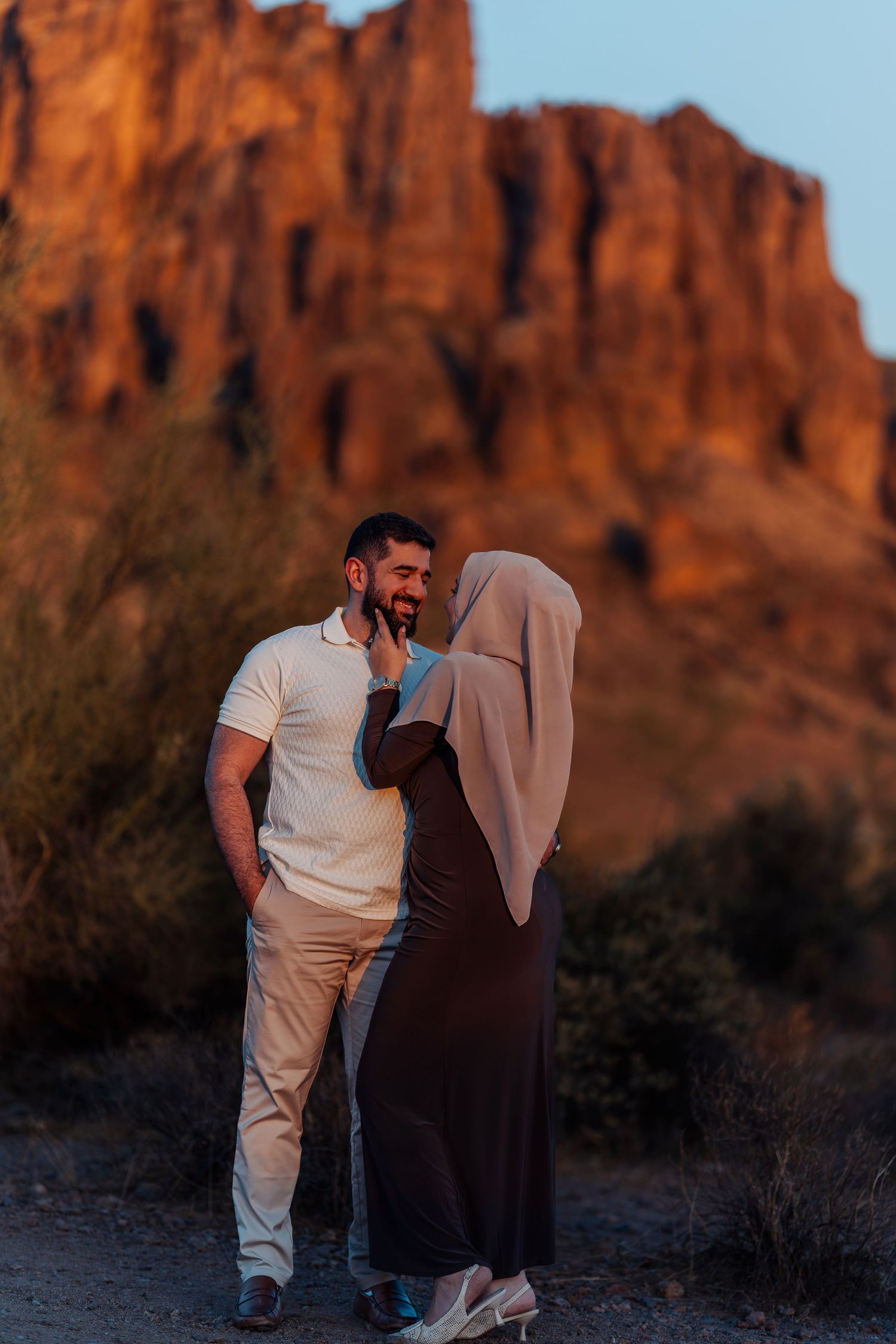 Muslim couple laughing together at sunset with dramatic red rock cliffs in the background.