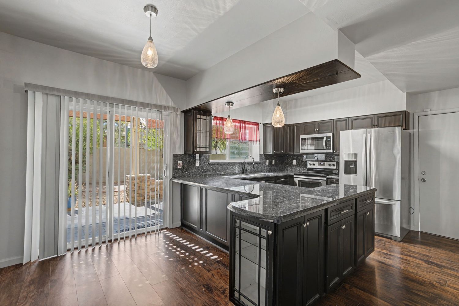 Modern kitchen with dark cabinetry, granite island, stainless steel appliances, and sliding glass doors to patio.