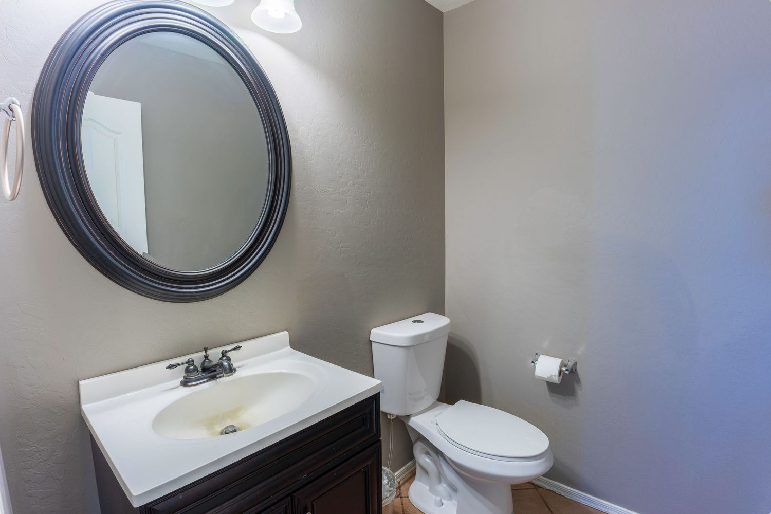 Clean half bathroom featuring dark vanity, oval mirror, white toilet, and neutral gray walls.