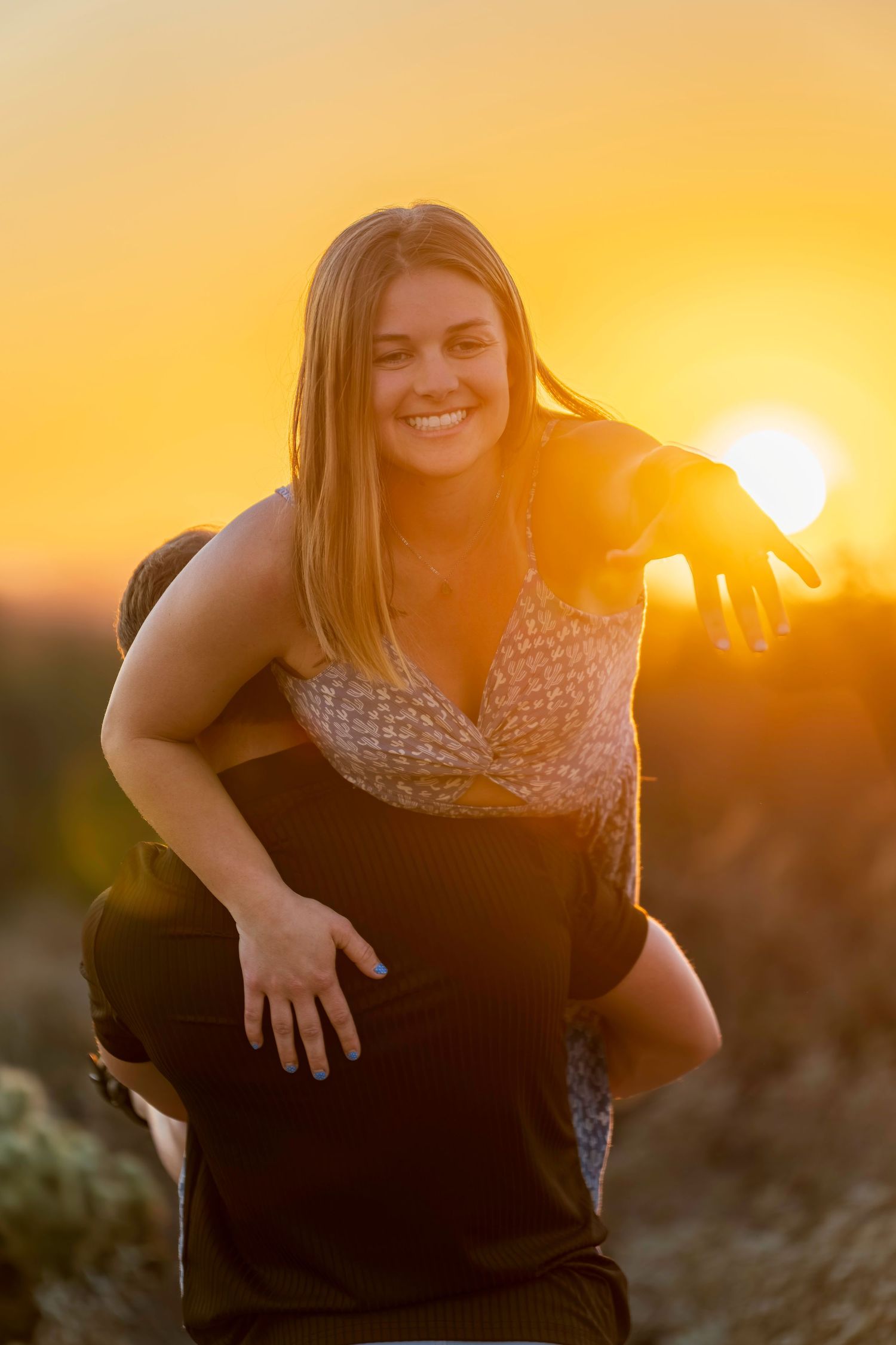 Joyful woman being carried piggyback by partner during golden sunset outdoors.