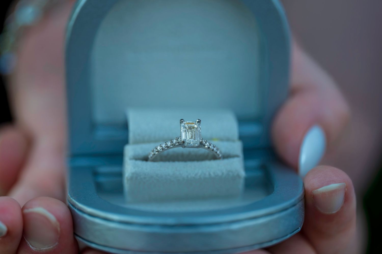 A sparkling princess-cut diamond engagement ring displayed in an open light blue velvet ring box.