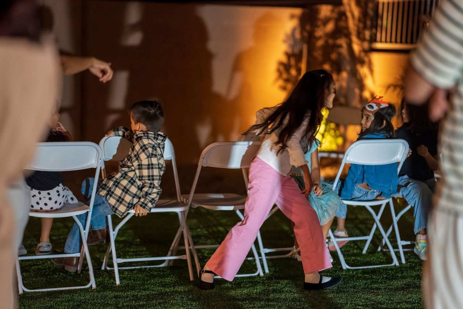 Children in casual attire sit on blue folding chairs at outdoor gathering.