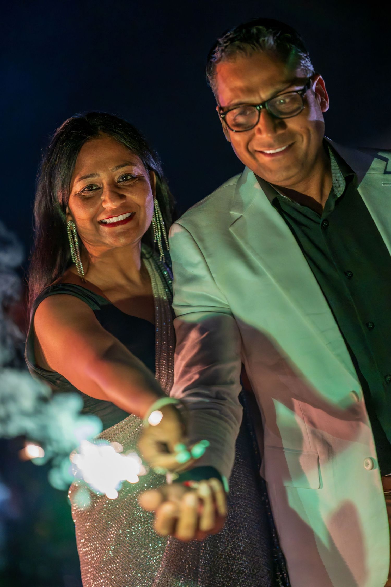 A couple smiling while holding sparklers during an evening celebration.