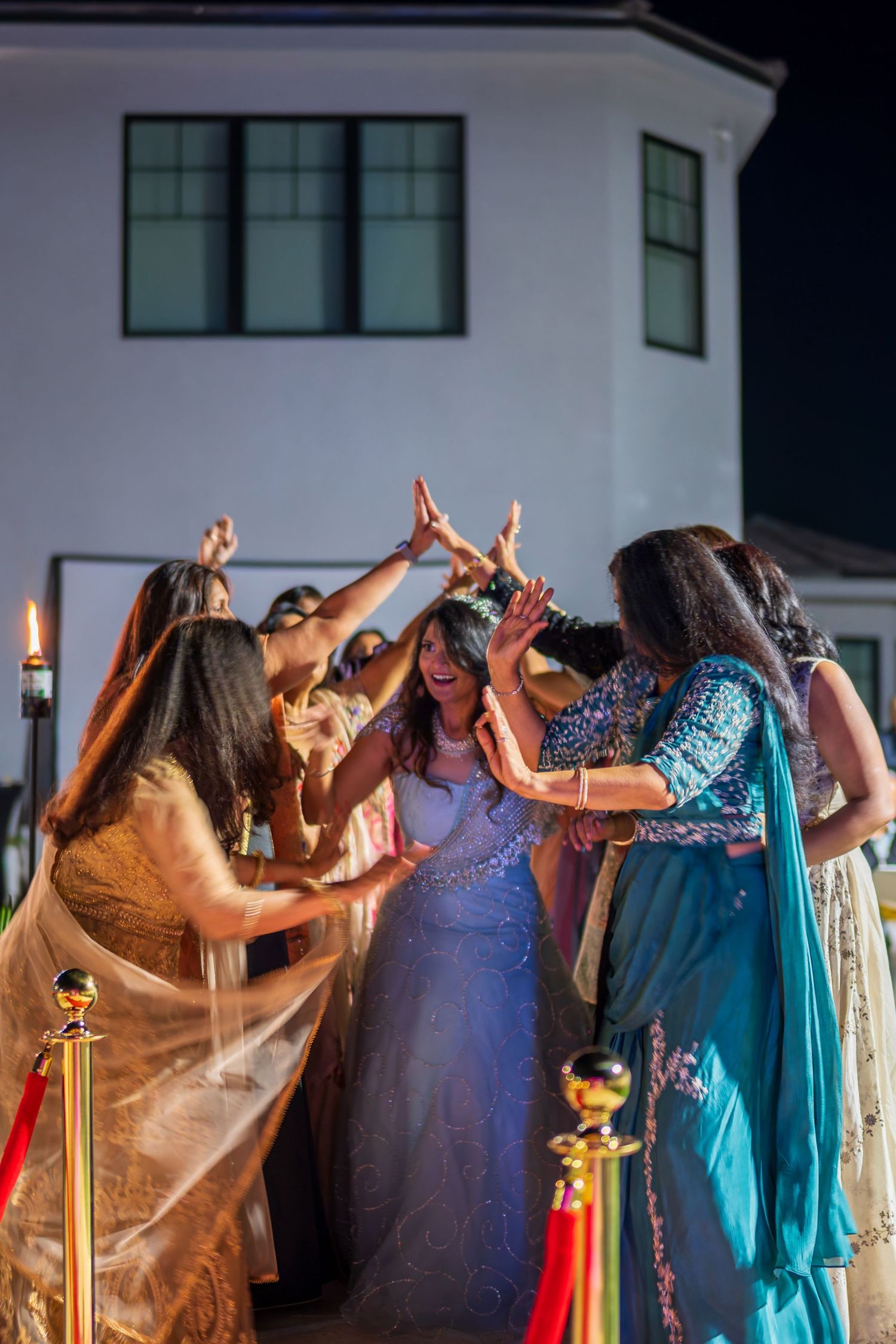 People in elegant dresses stand together with raised arms during a nighttime celebration.