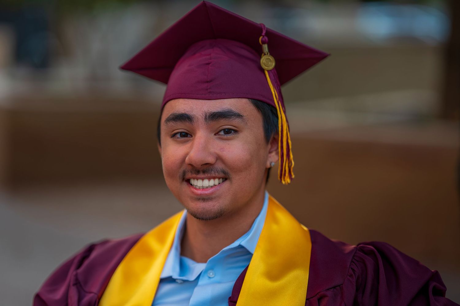 Graduate in maroon cap and gold stole smiling during graduation ceremony.