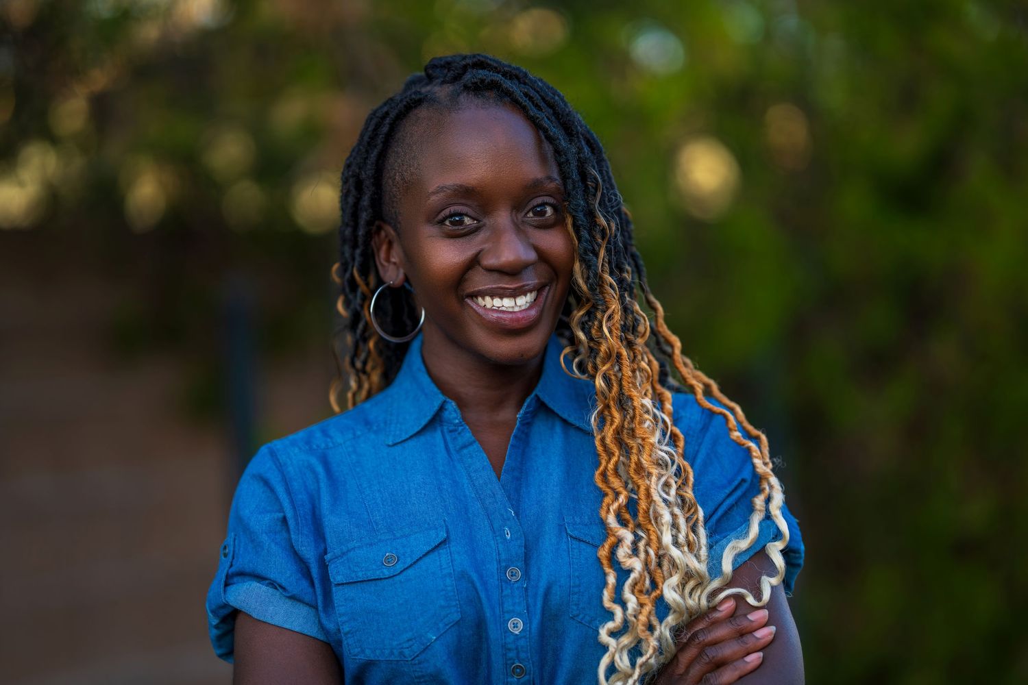Person in bright blue denim shirt with blonde and dark braided hair smiling outdoors.