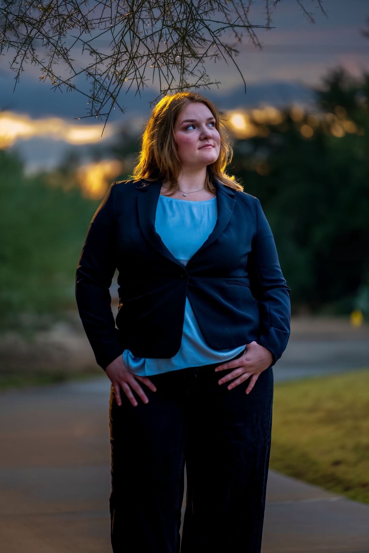 Person in professional attire strikes a casual pose on a path during golden hour.