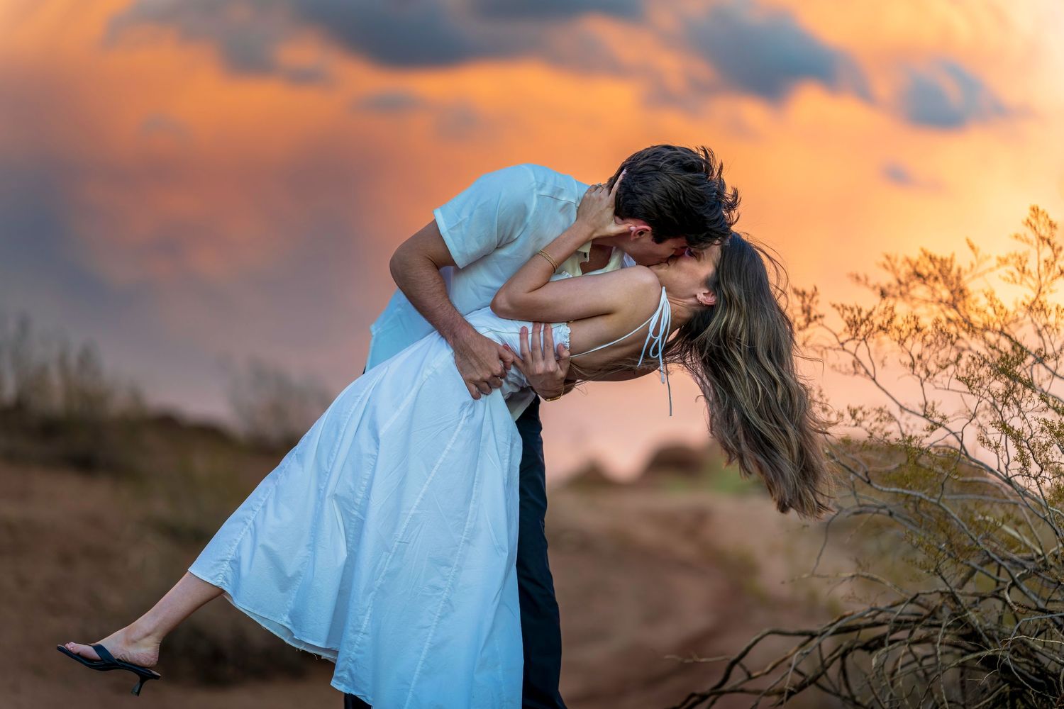 Dramatic dip pose between a couple during golden hour with desert landscape backdrop.