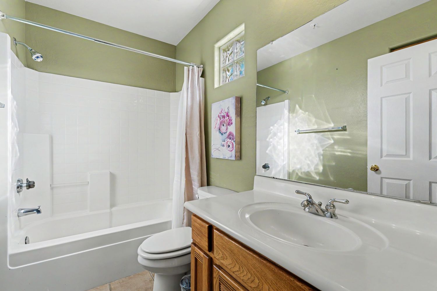 Full bathroom with single vanity, large mirror, tub-shower combo, and green walls in a residential home.