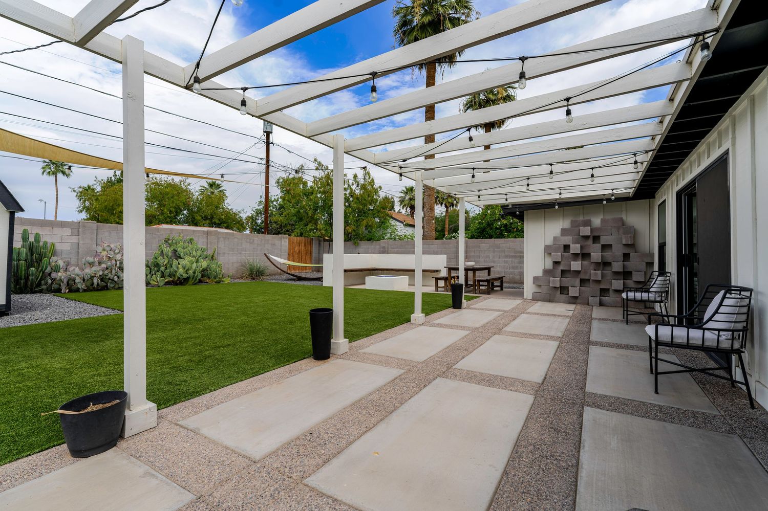 Modern pergola patio with string lights, large pavers, lush lawn, hammock, and outdoor seating area.