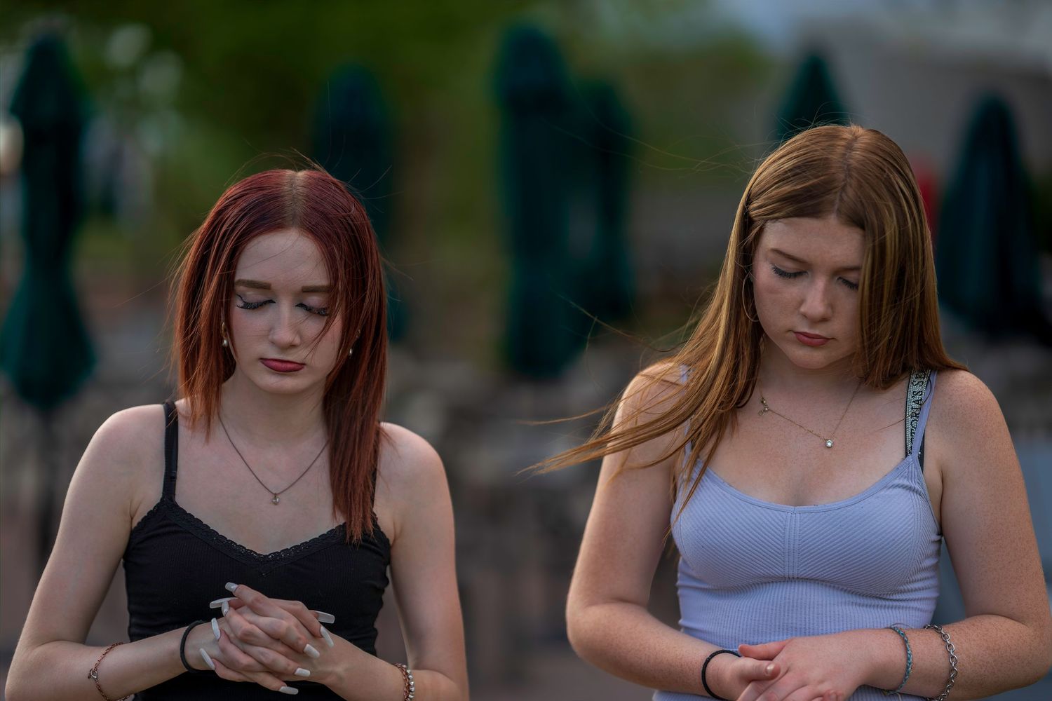 Two young women with red and auburn hair looking down at their phones outdoors.