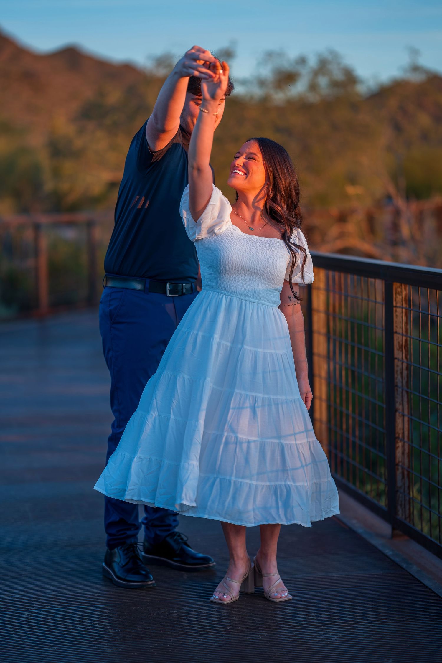 A romantic desert photoshoot featuring a couple in black and white outfits during sunset.