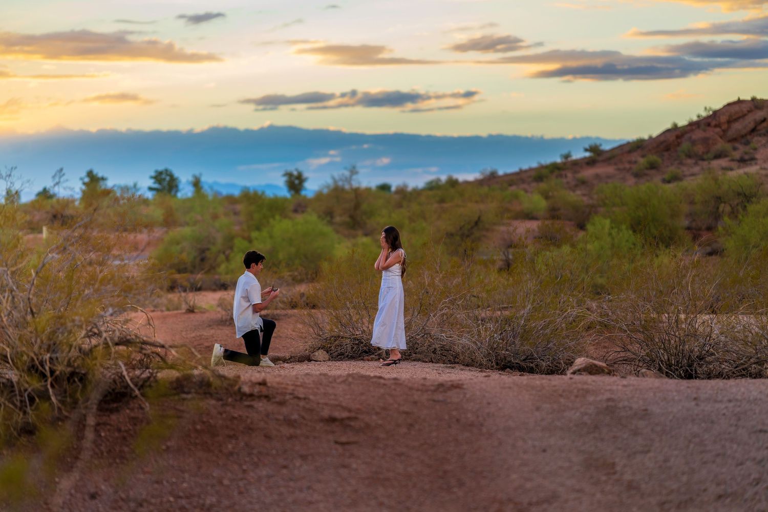 A couple stands together against a desert landscape during a golden sunset.