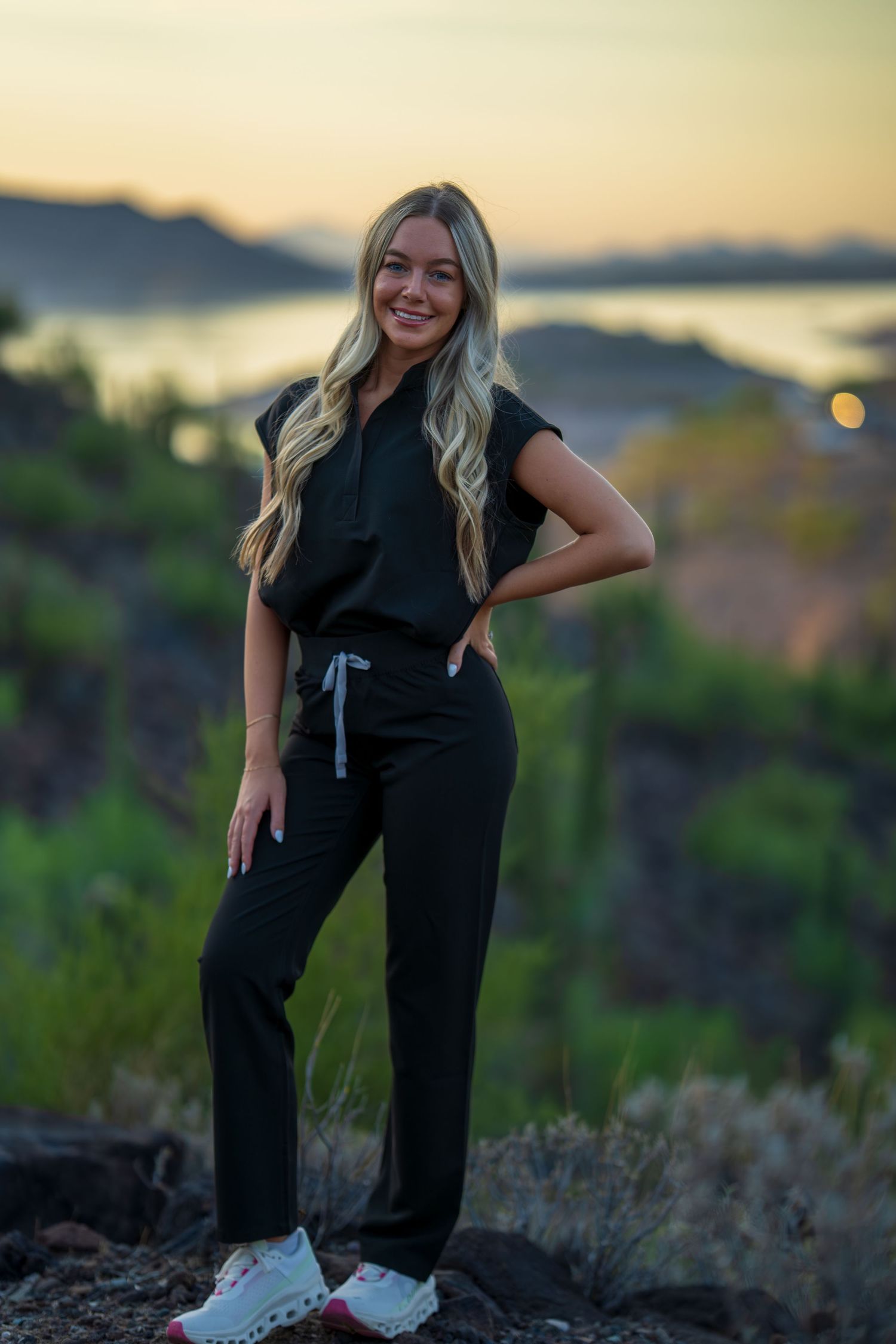 Medical worker in dark scrubs smiles during golden hour photoshoot in desert landscape.