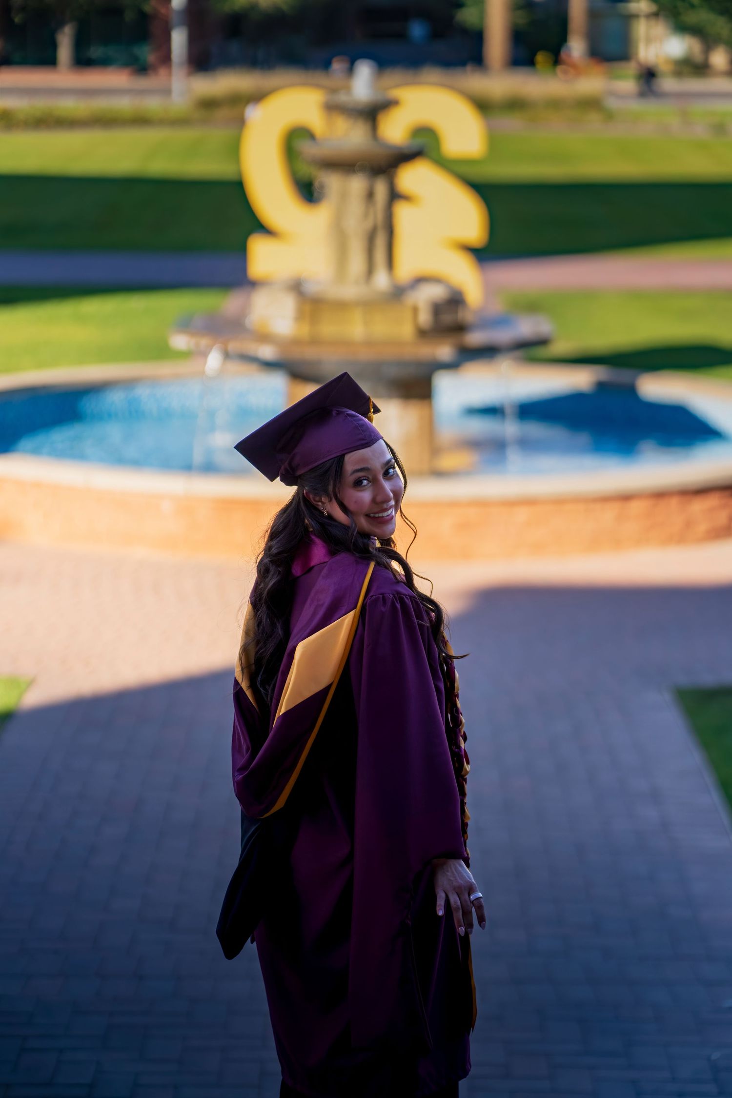Graduate in purple cap and gown walking outdoors with decorative stoles against blurred background.