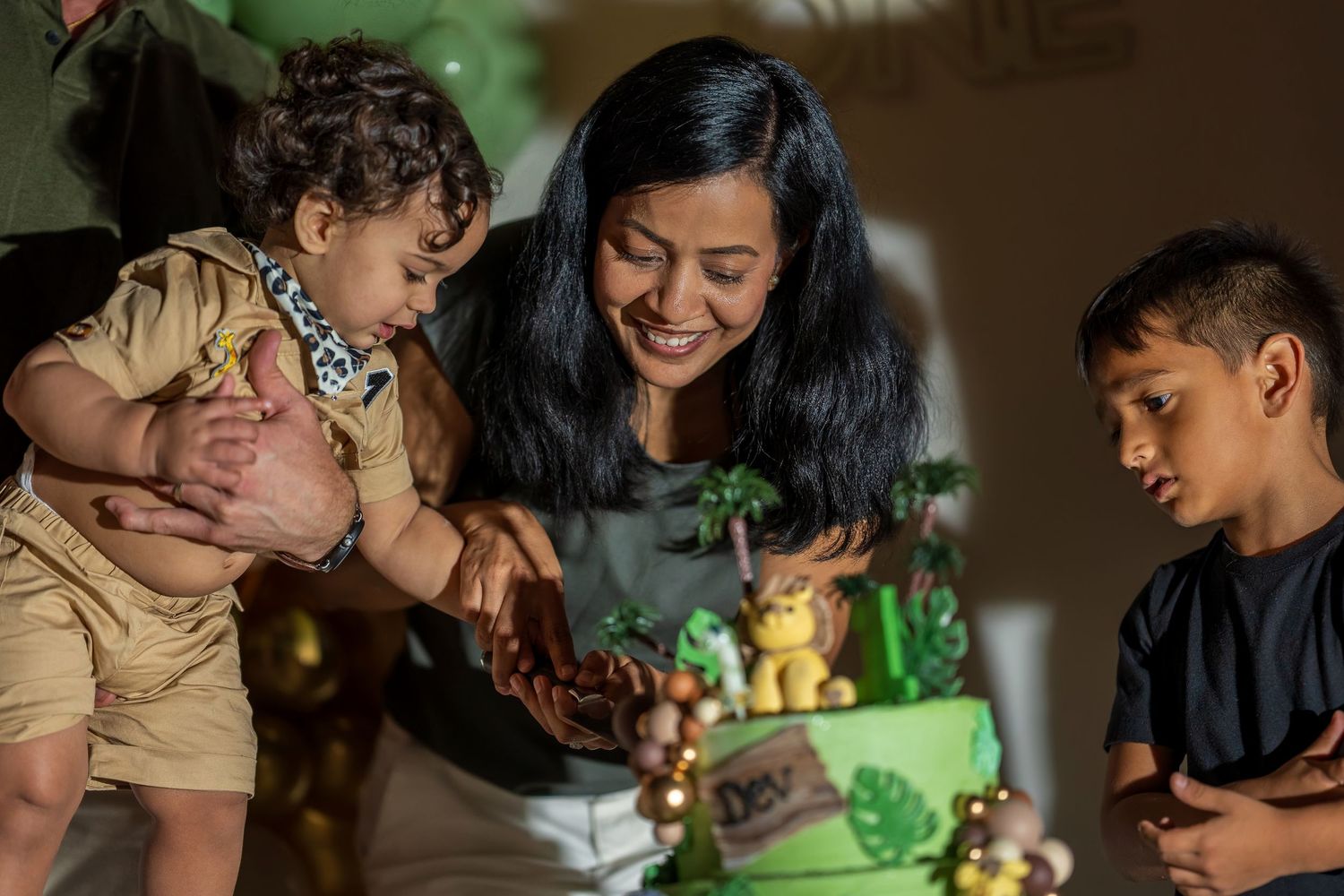 A joyful family gathering around a green safari-themed birthday cake during a celebration.