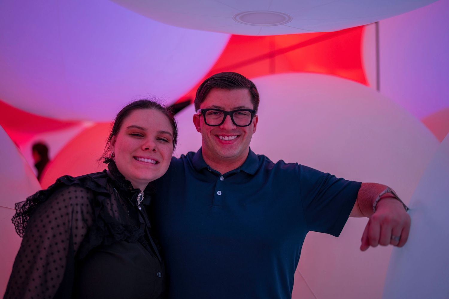 Two smiling friends pose together in a colorful red and white illuminated art installation.