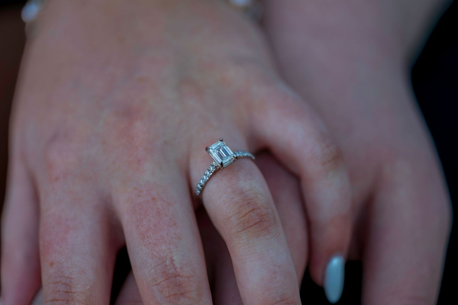 Close-up of a hand wearing a stunning emerald-cut diamond engagement ring with a pavé band.