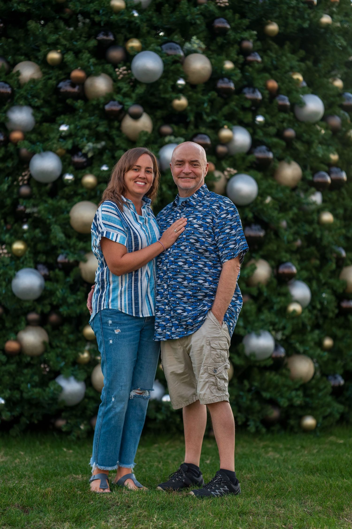 Couple sharing a playful moment in front of decorated Christmas tree.