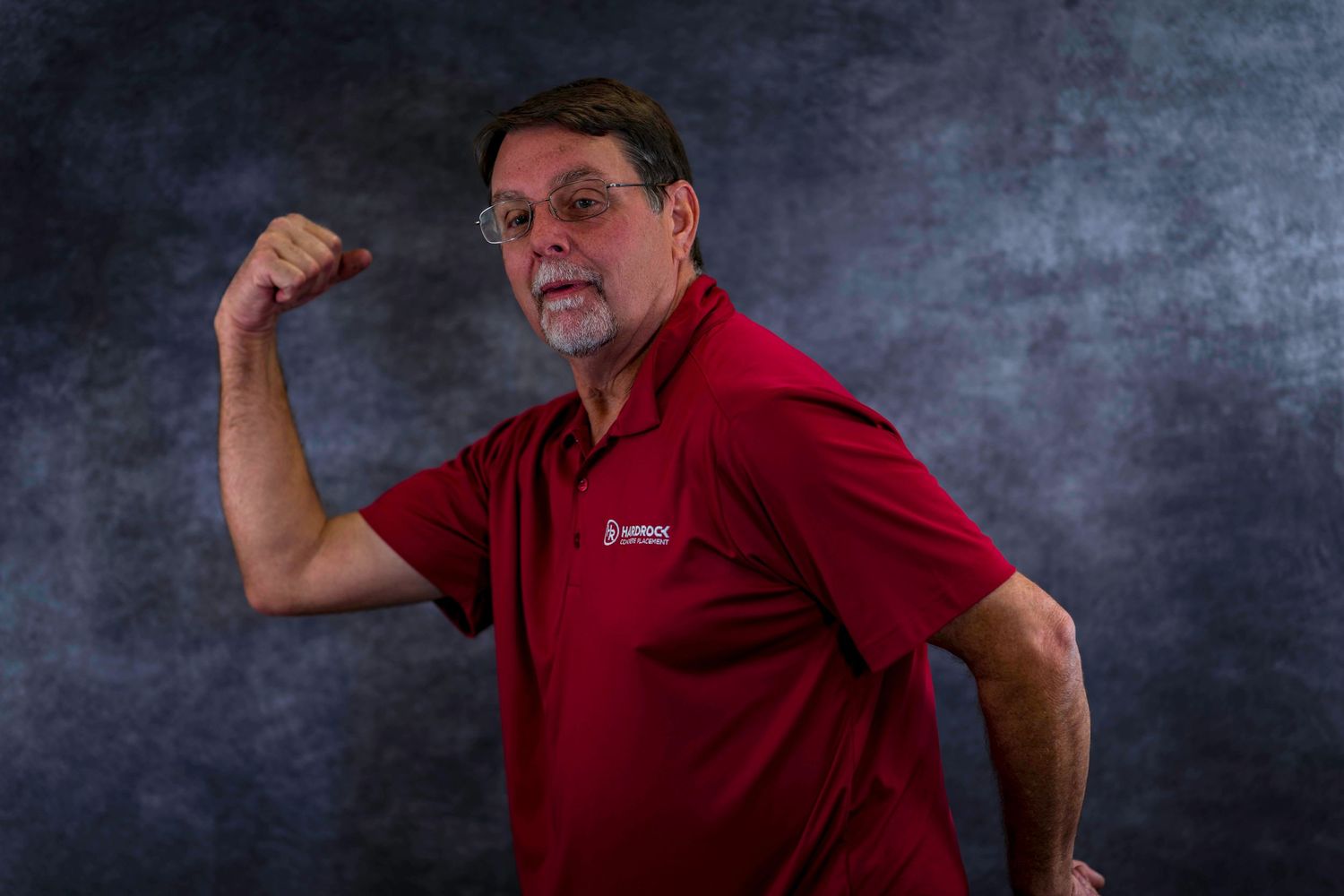 Person in red polo shirt flexing arm muscle against gray background.