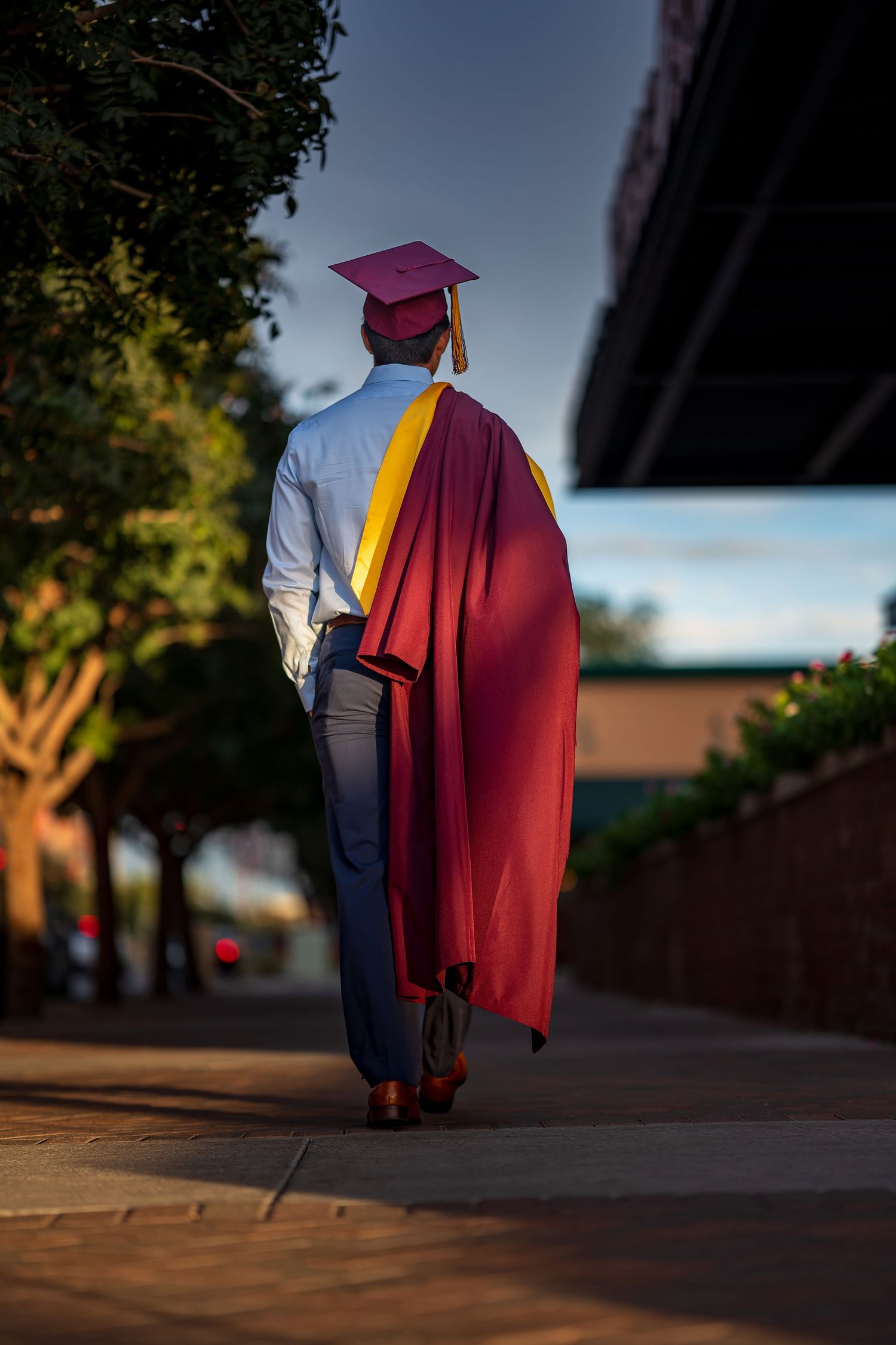 Graduate walking away in maroon cap and gown during sunset.