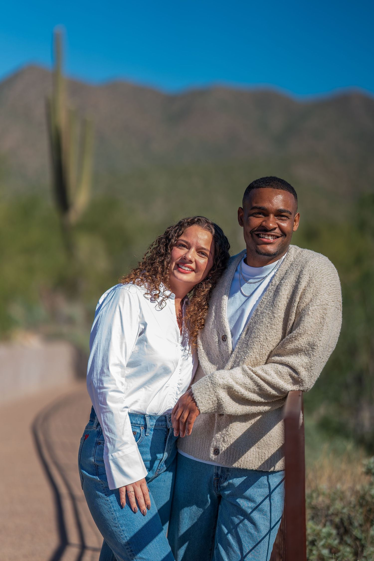 A couple poses together on a desert trail with saguaro cactus in the background.