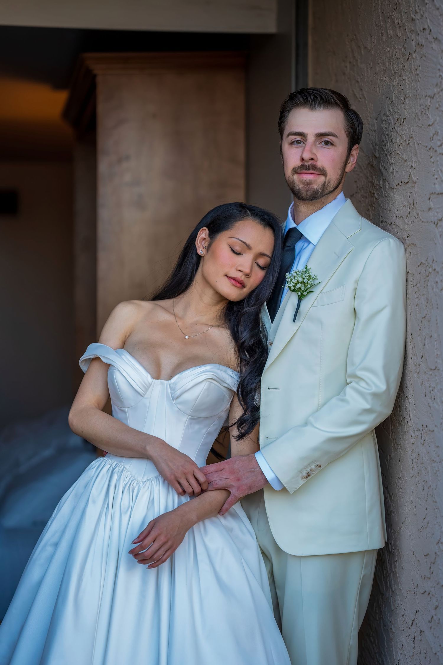 A tender moment between newlyweds in classic wedding attire against a neutral background.