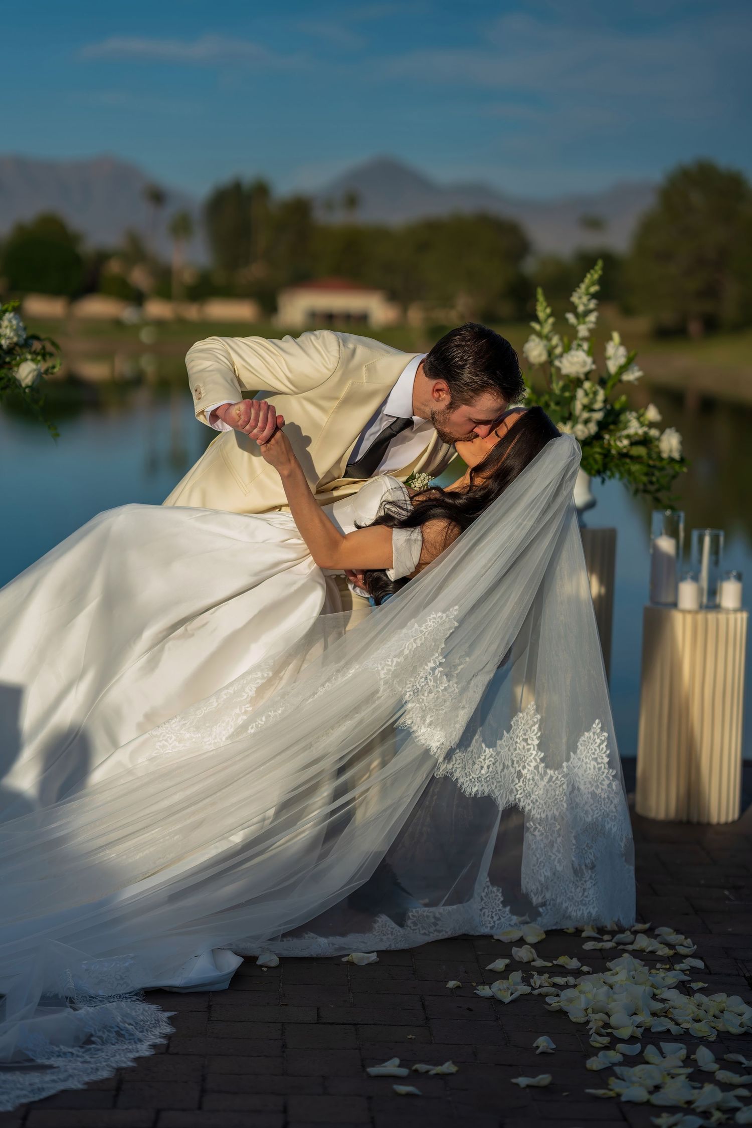 A dramatic dip pose during wedding portraits by a lakeside with mountains in the background.
