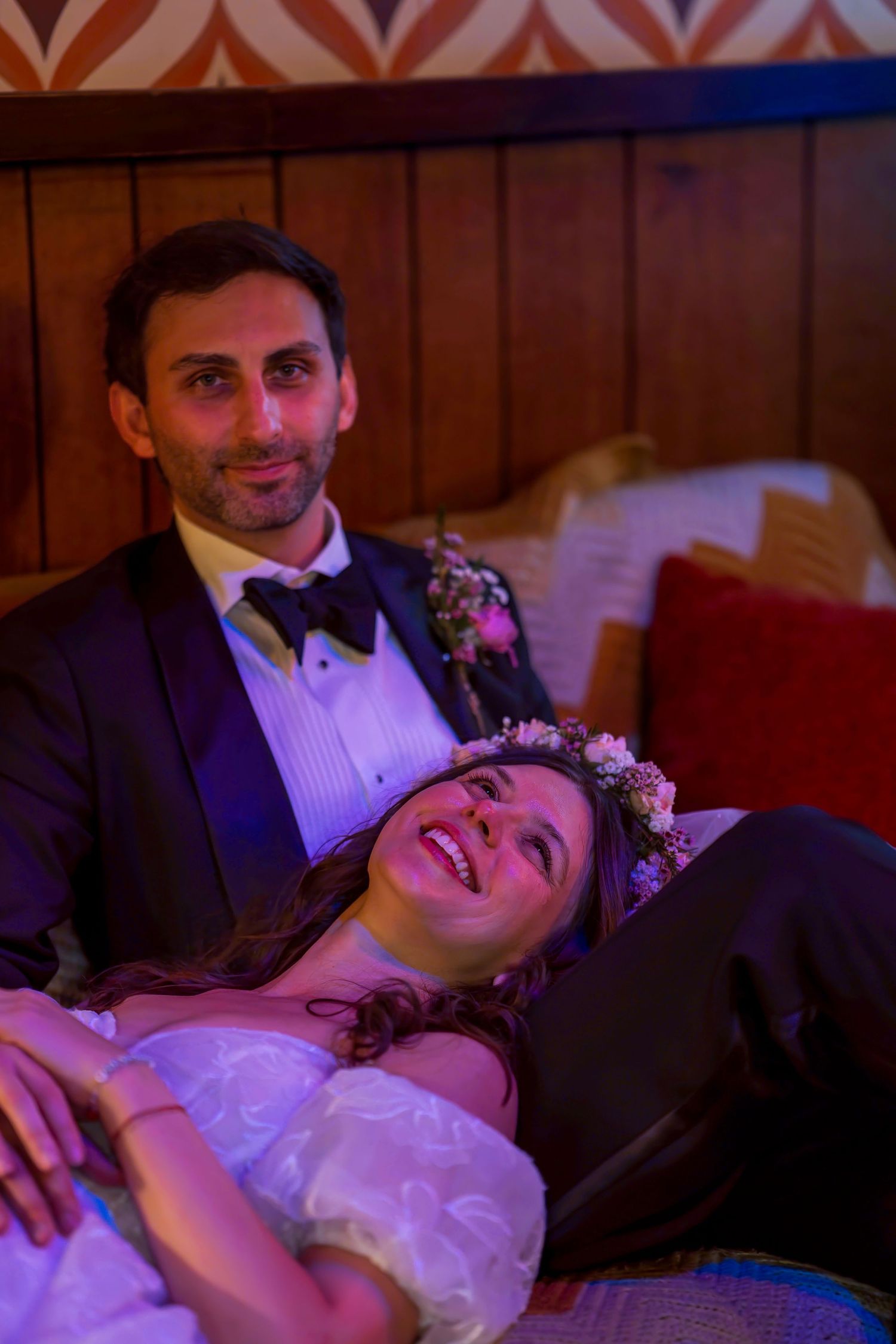 Bride and groom relaxing together at their wedding reception, bride wearing a floral crown smiling joyfully.