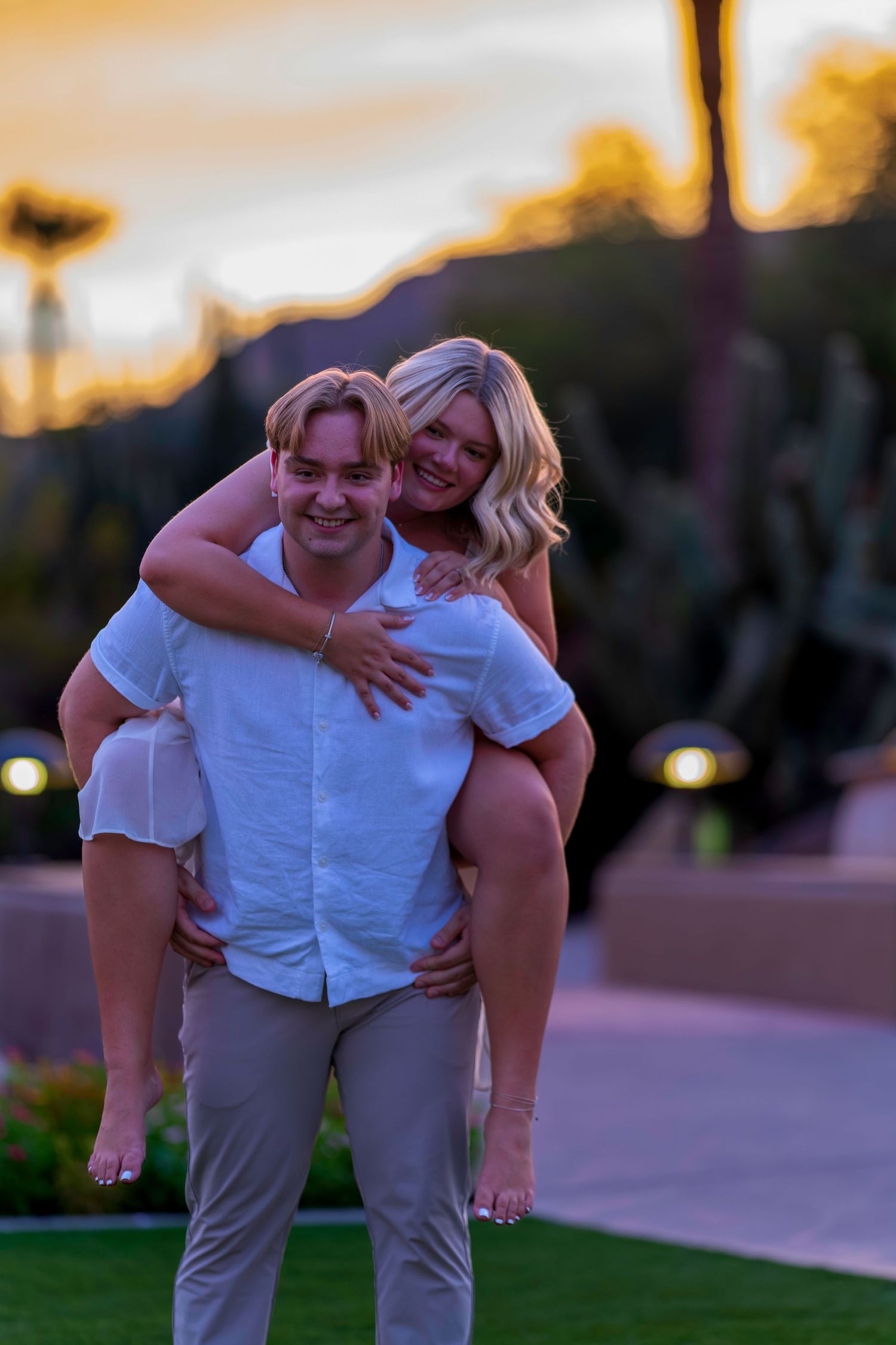 Young man giving blonde woman a piggyback ride outdoors at sunset.