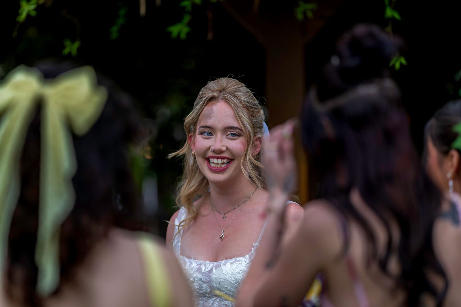 Smiling bride in white dress surrounded by bridesmaids in yellow at an outdoor wedding celebration.