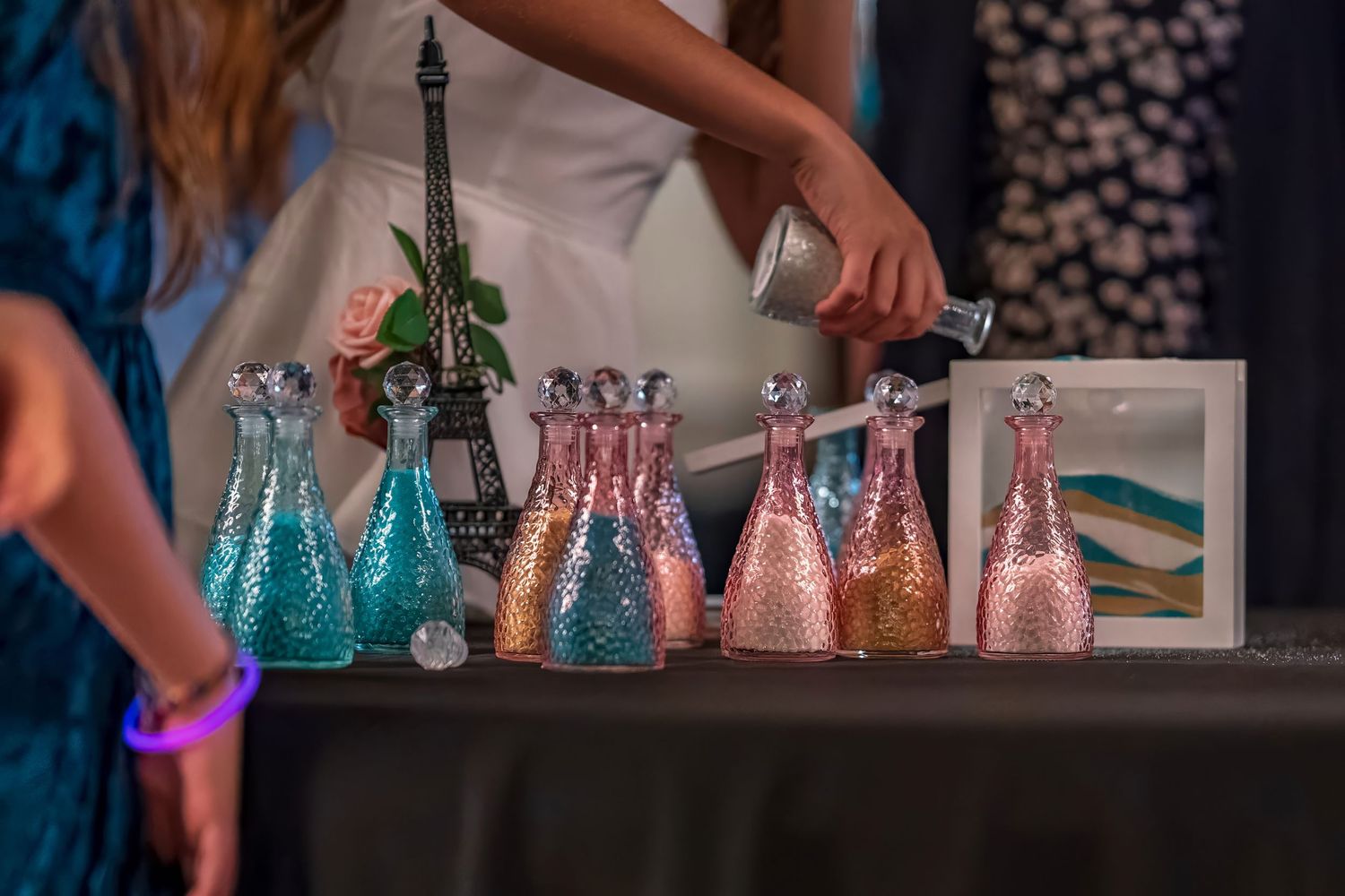 Colorful glitter bottles displayed on a table with an Eiffel Tower figurine at a Paris-themed party event.