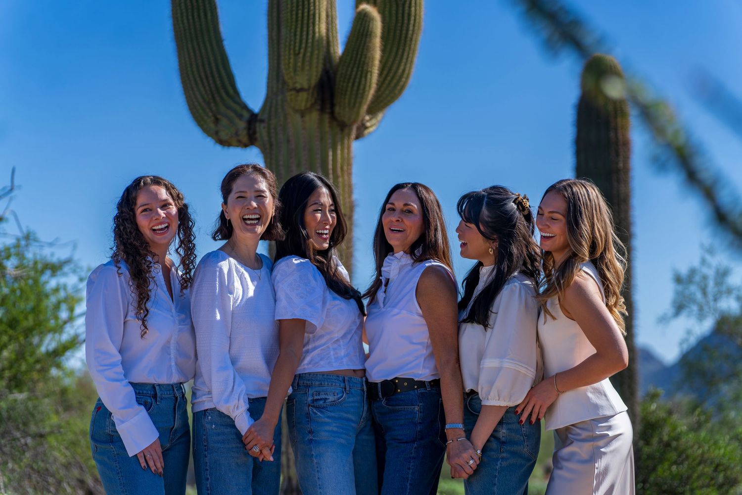 Friends in matching outfits gathered around saguaro cactus for photo.