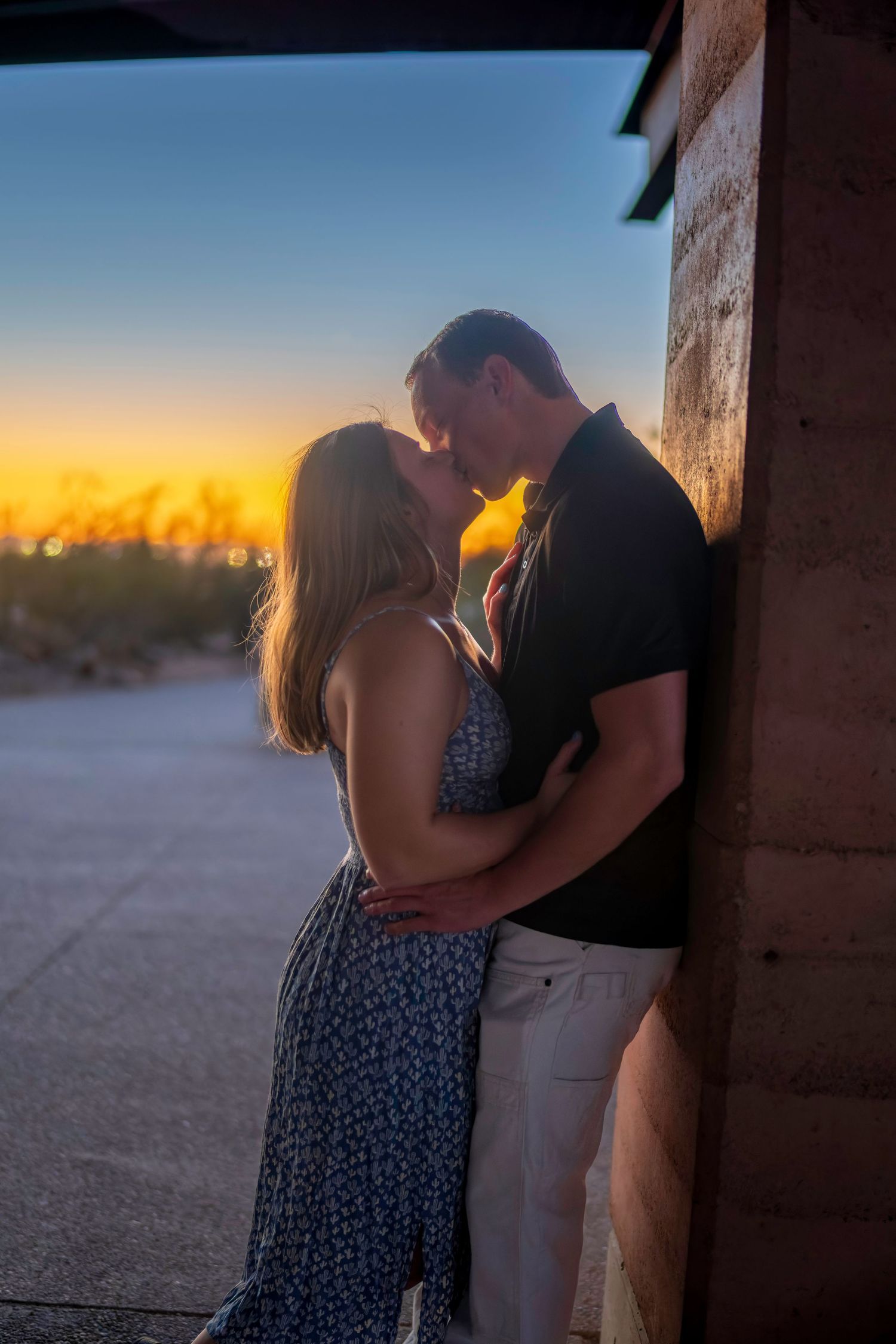 Couple kissing against rustic wall at twilight with stunning golden blue sunset sky in desert background.
