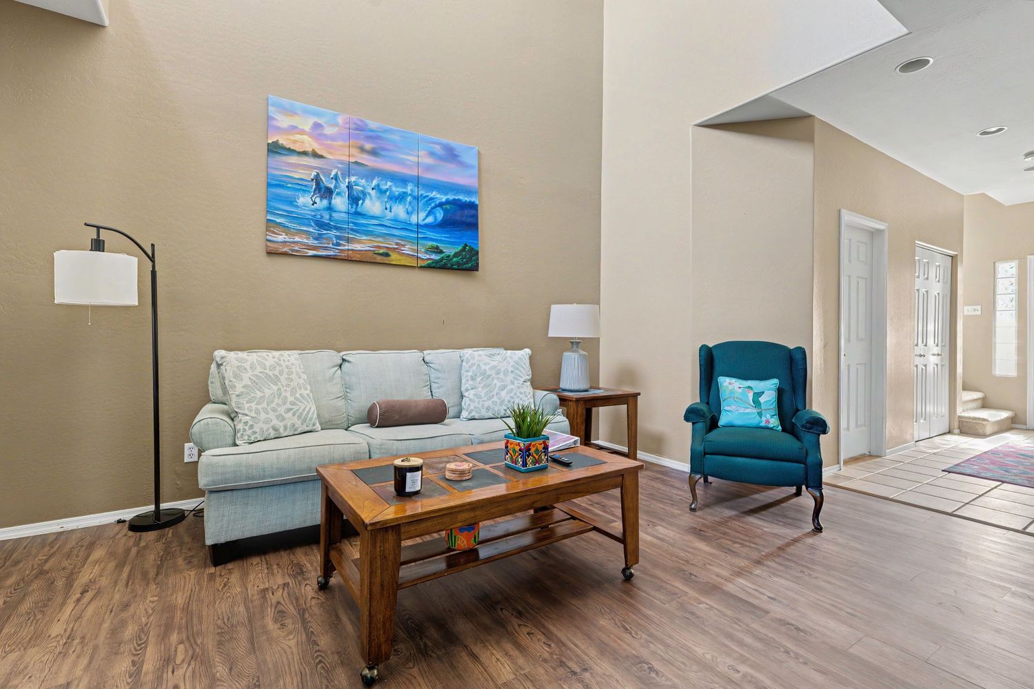 Cozy living room with light sofa, teal accent chair, wood coffee table, and vibrant wall art above.