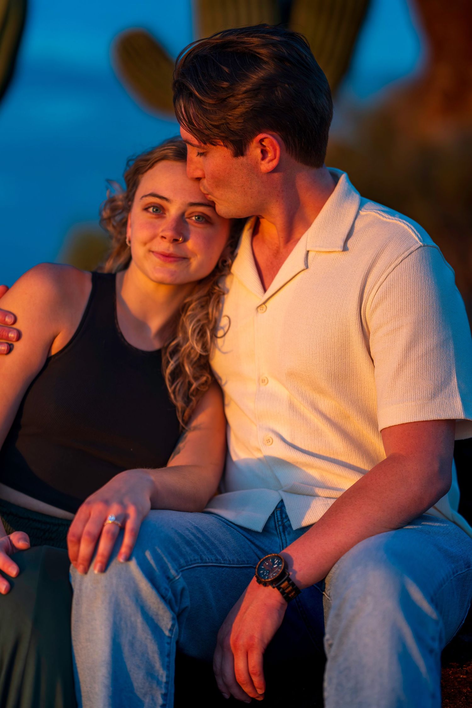 Couple sharing a tender kiss at sunset near saguaro cacti in the Arizona desert.